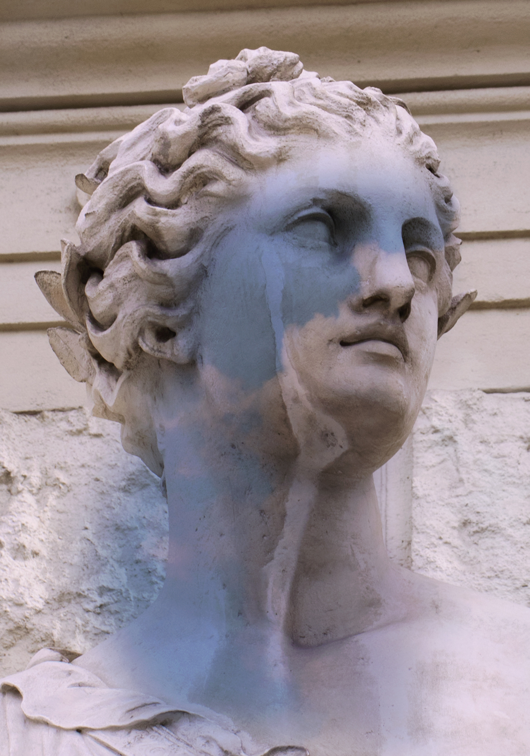 a close up of an old statue face; part of it is stained a baby blue colour