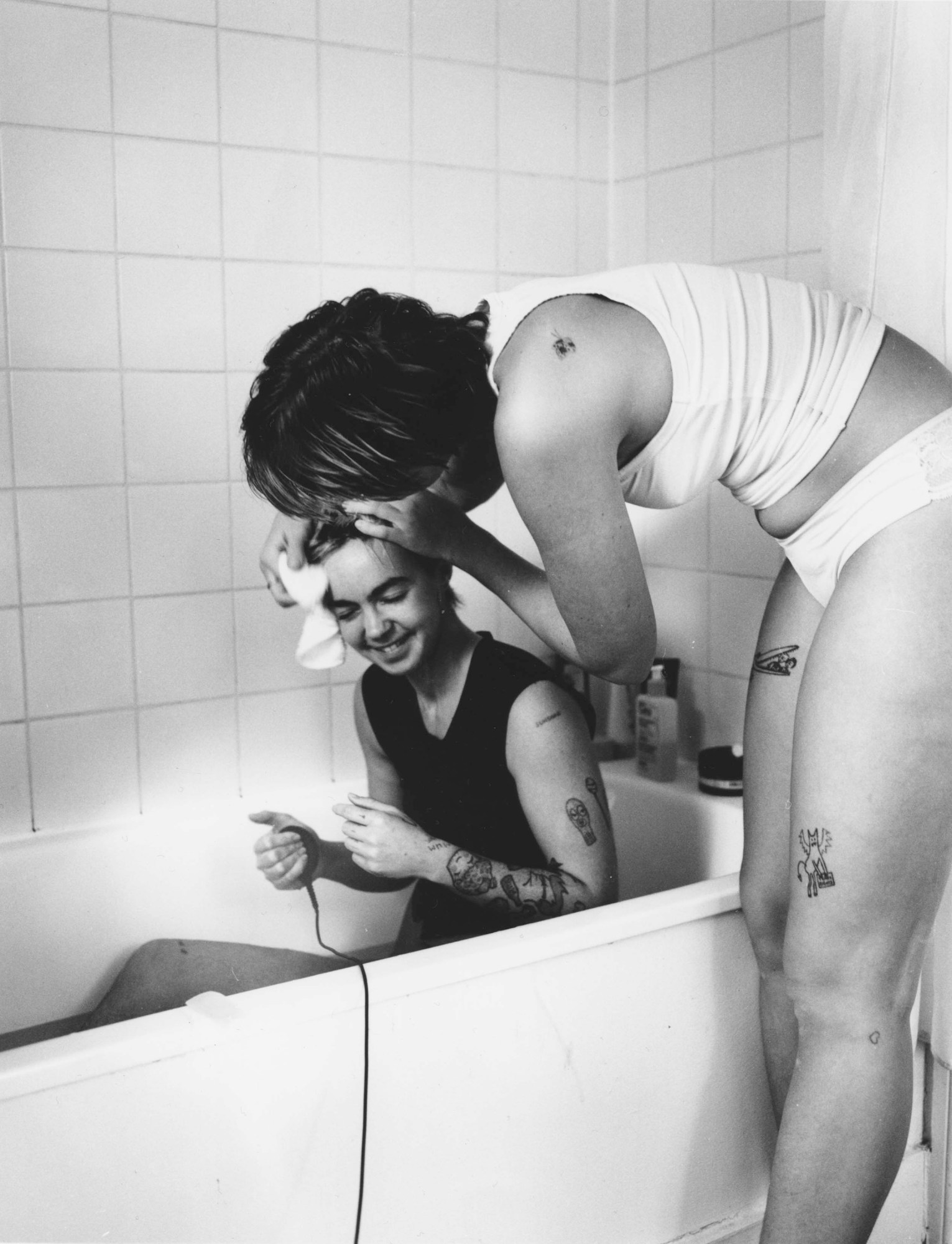 the photographer jesse glazzard sitting in a bath having his hair washed by his partner; he uses a shutter release cable to take the portrait