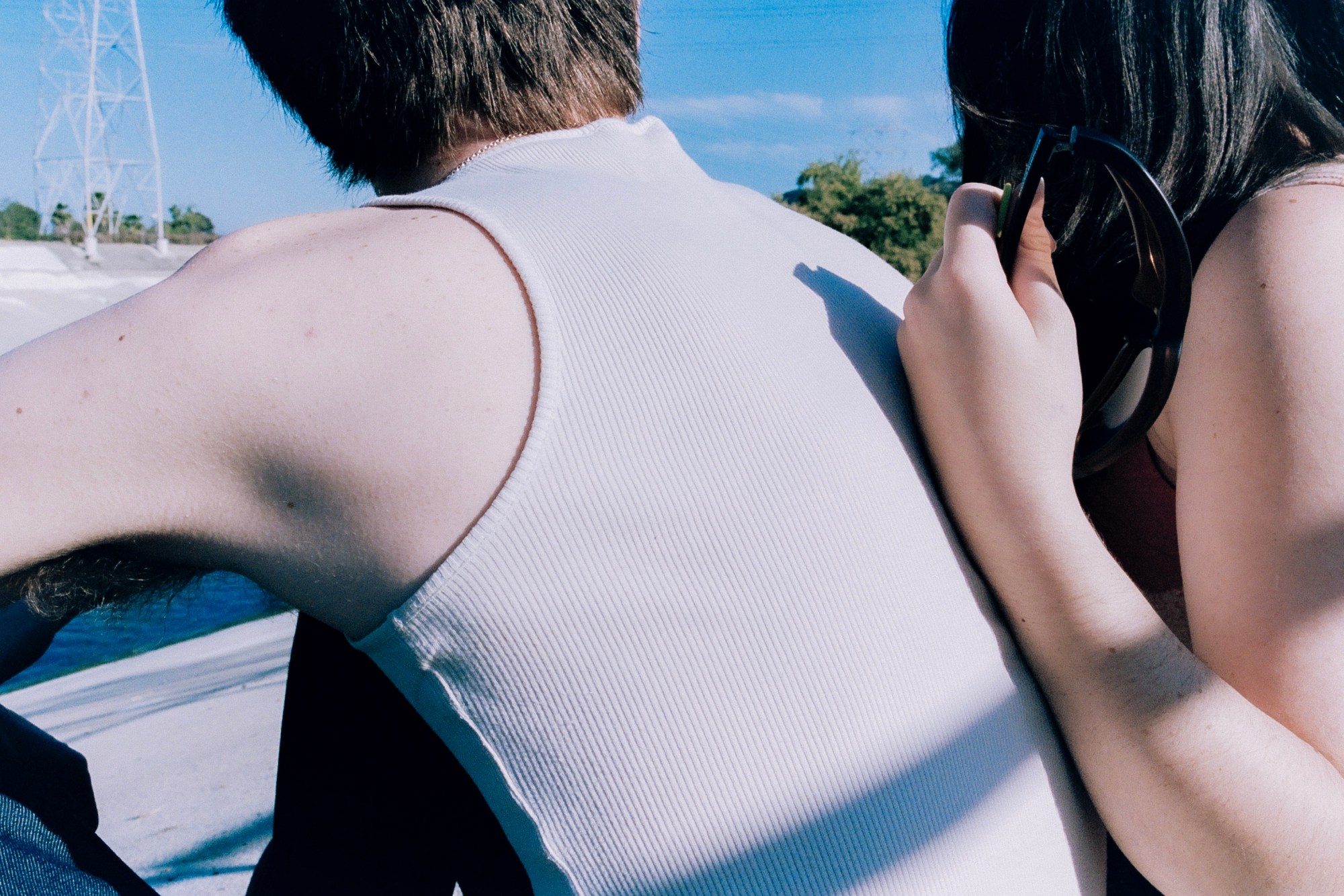 two people with their backs to the camera, one wearing a white tank top