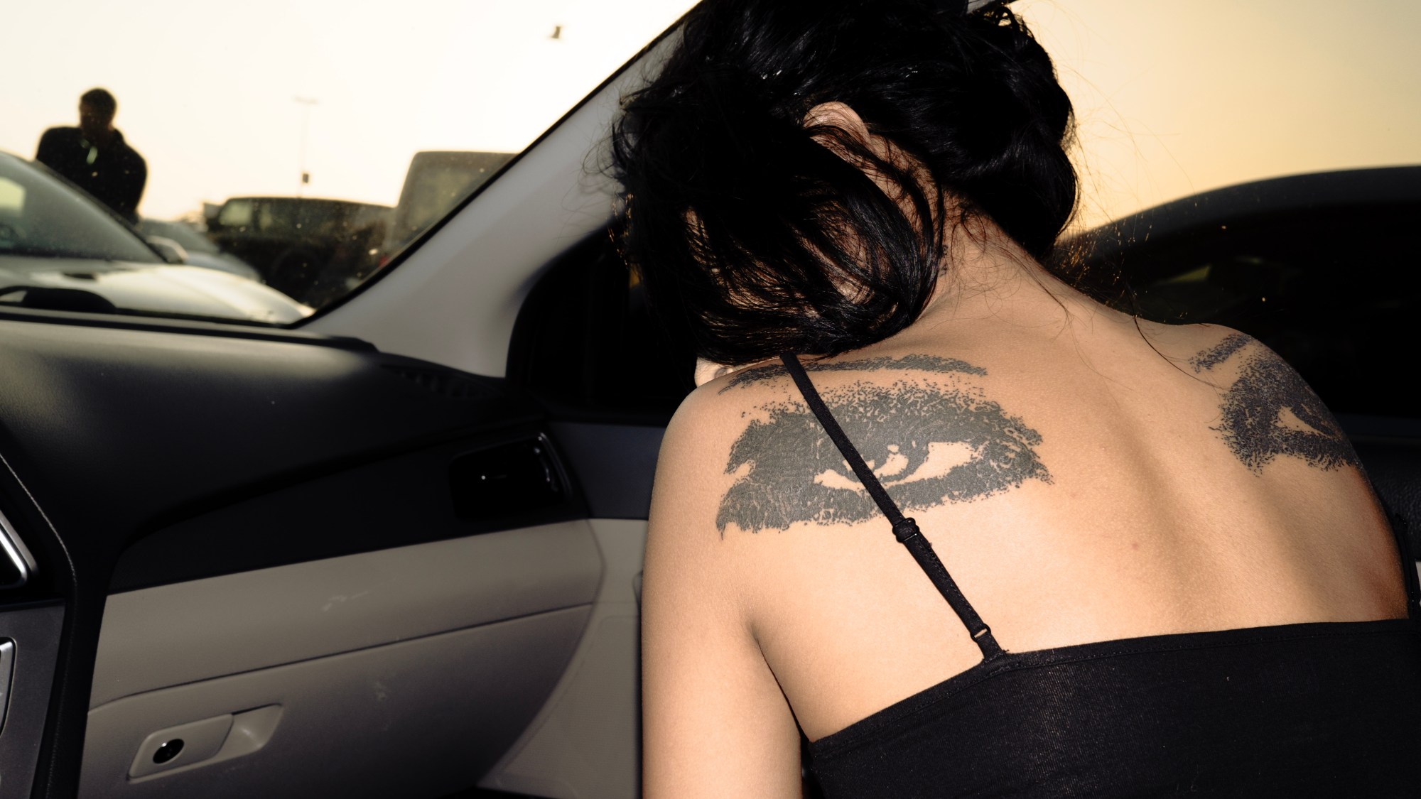 a woman in the front passenger seat of a car with black eye tattoos on her back