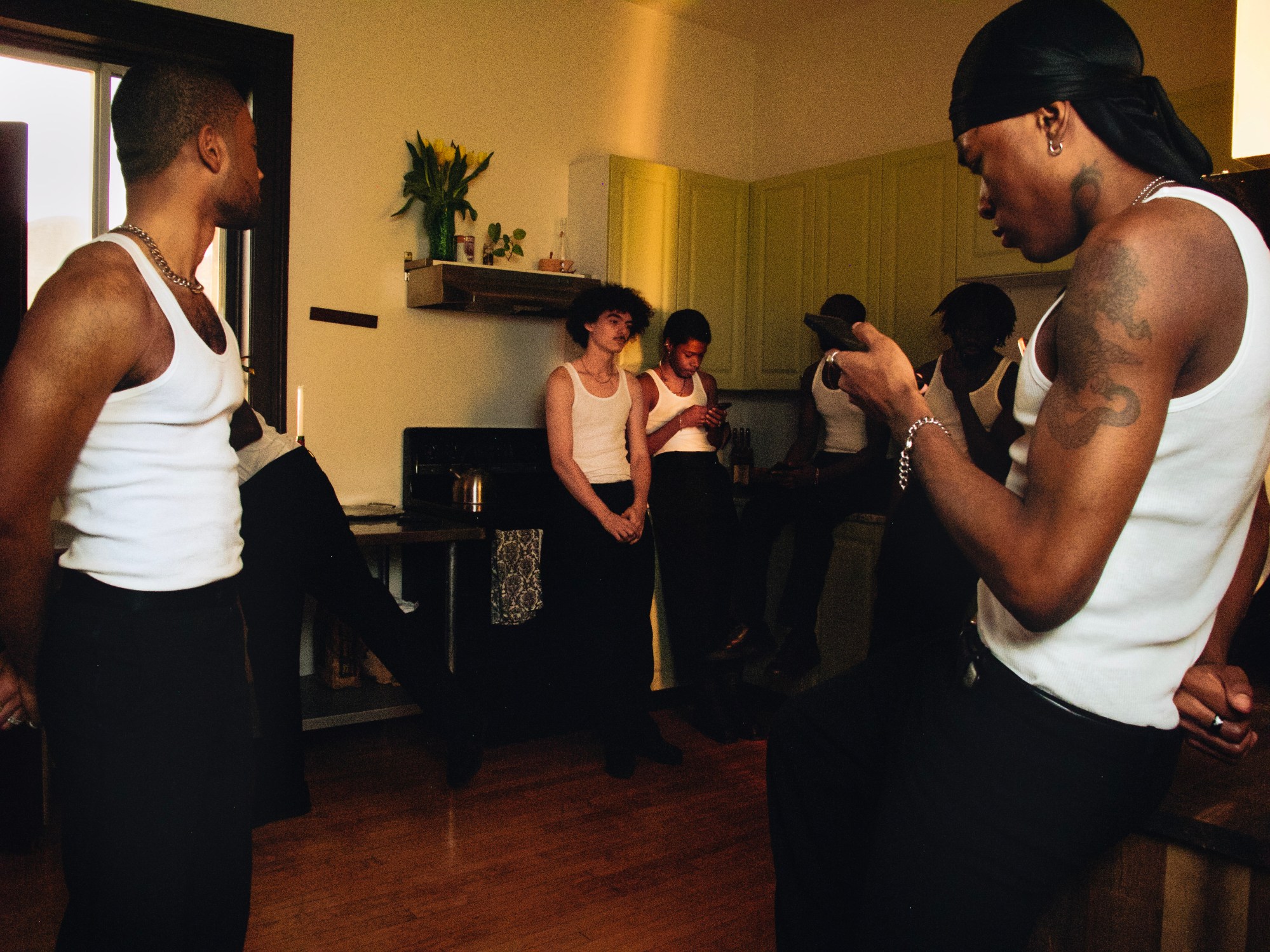 a group of men in white tank tops standing in a dimly lit kitchen