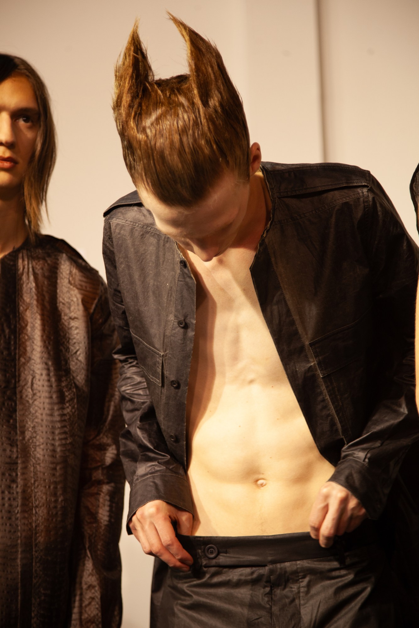 a model with sculpted hair looking down and holding his waistband