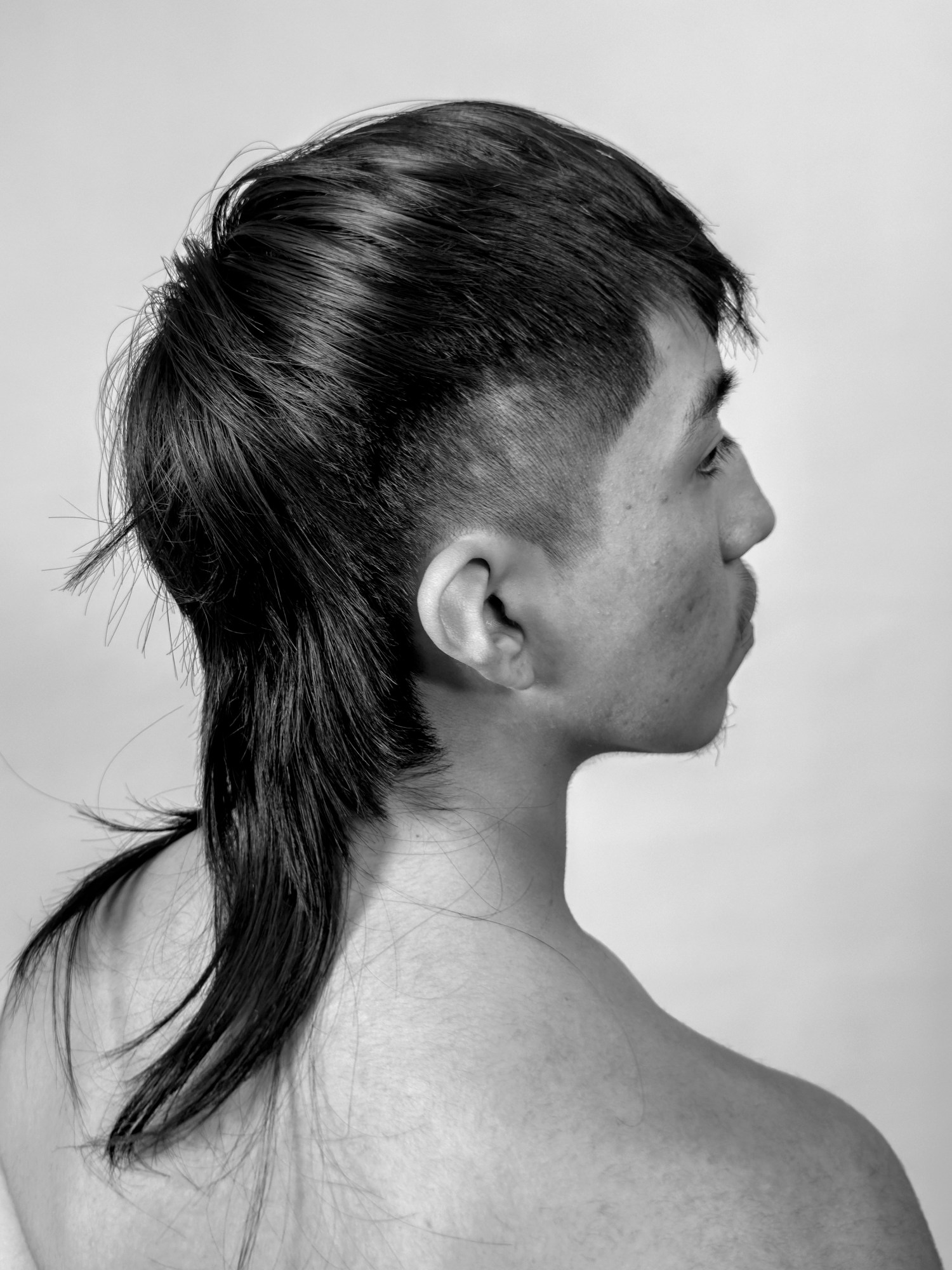 Black-and-white image of a man with a brunette mullet shot from behind