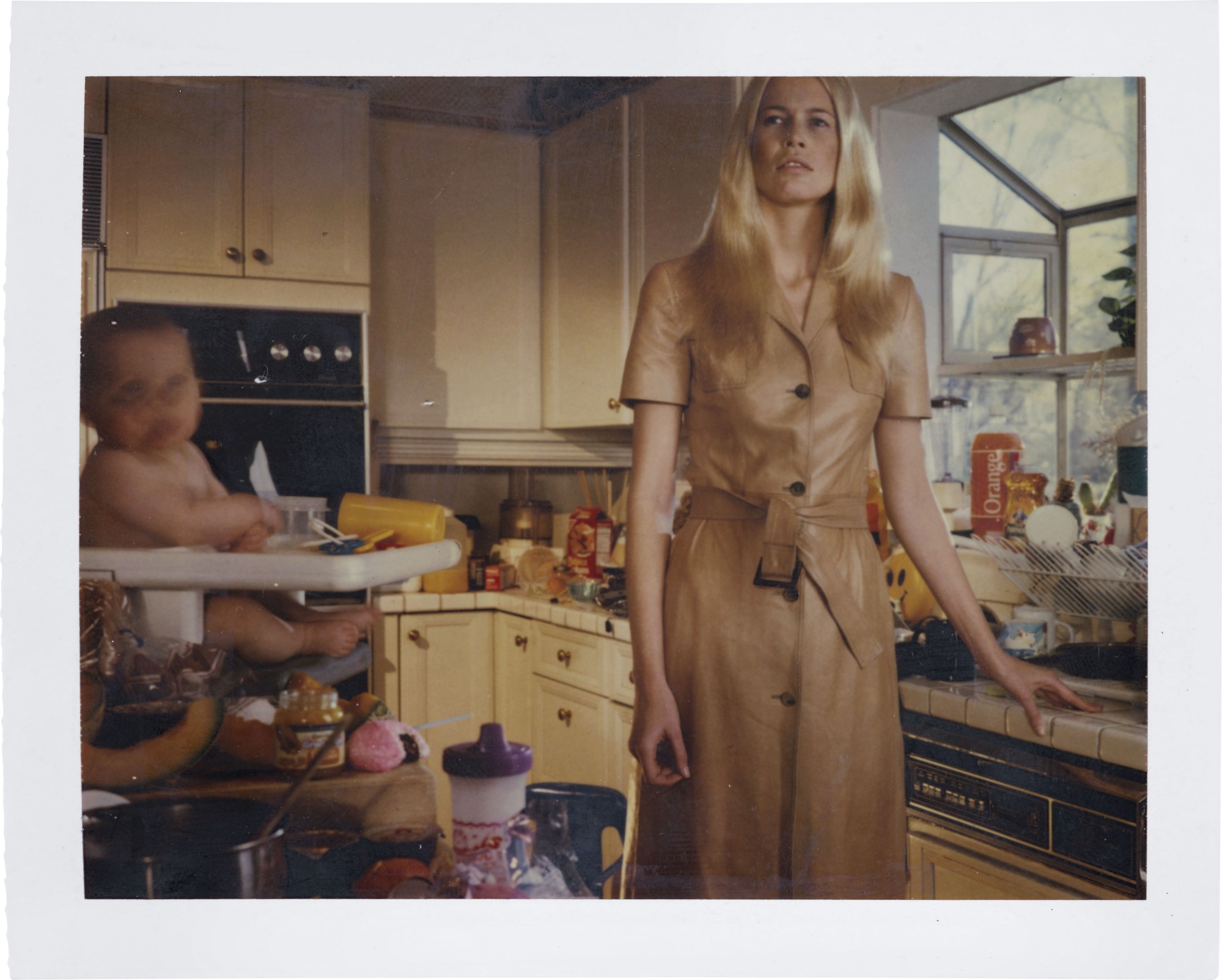 Claudia Schiffer in a messy kitchen with a baby in a high chair