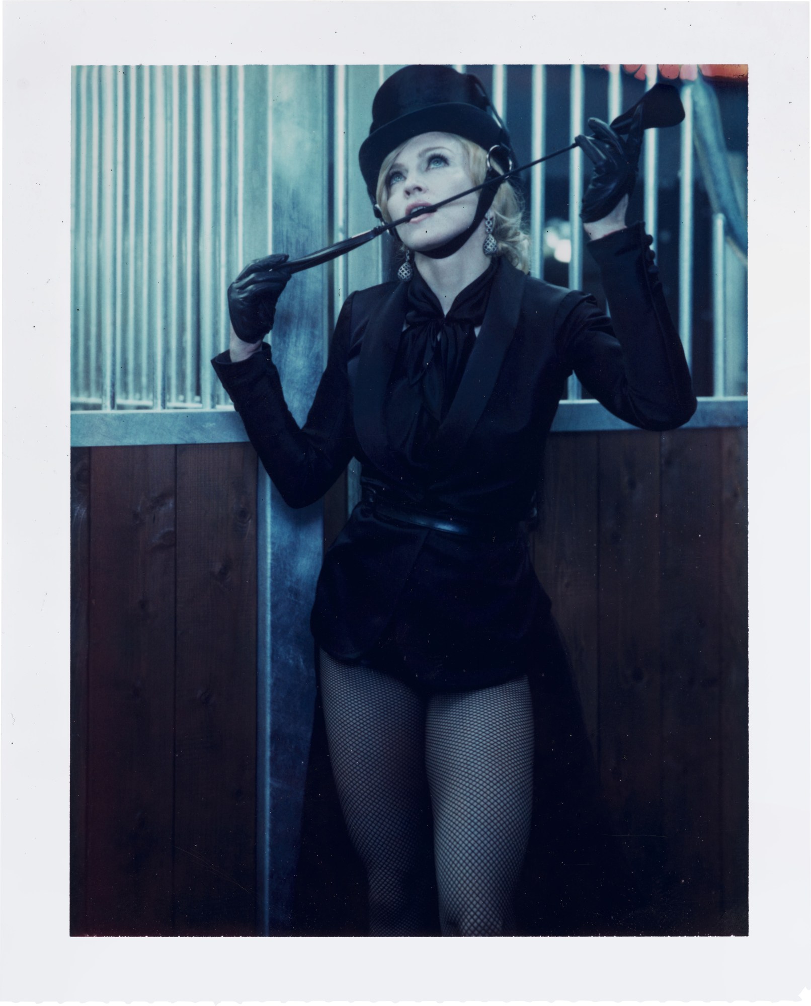 A polaroid of Madonna in fishnets biting a riding crop