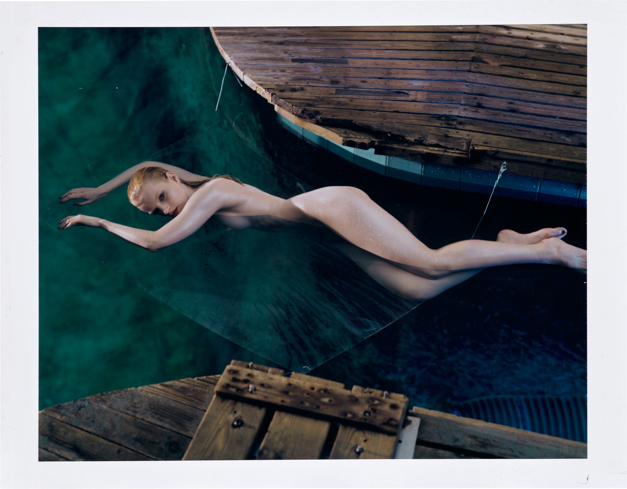 A naked woman lying in blue water between two wooden decks