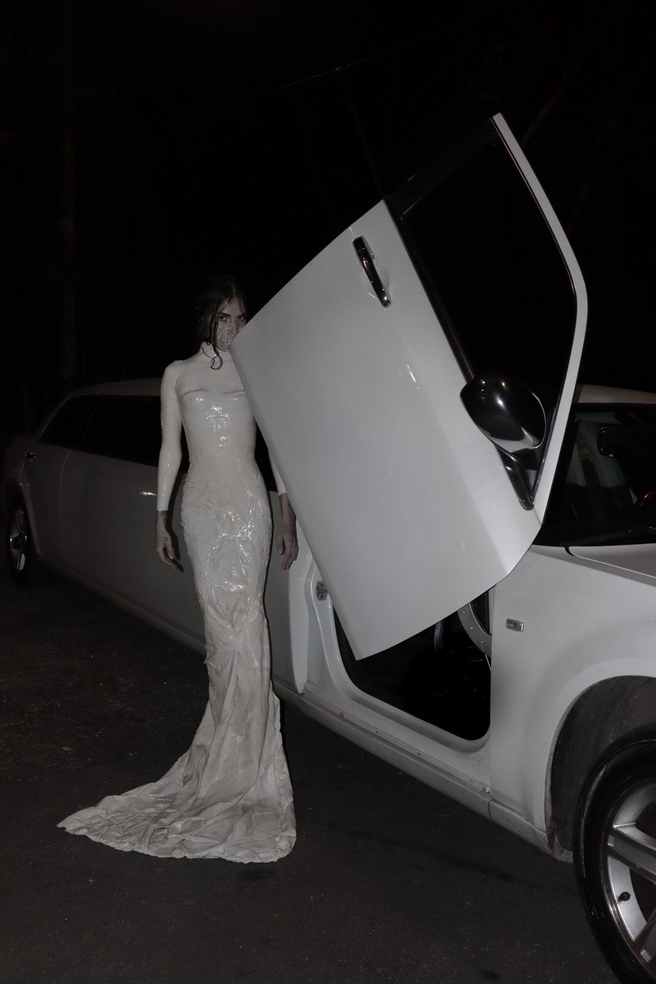 brazilian artist aun helden in a long white dress standing in front of a white car door