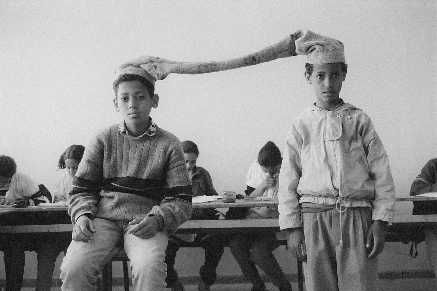 black-and-white photo of two students in a classroom joined at the head by a scarf