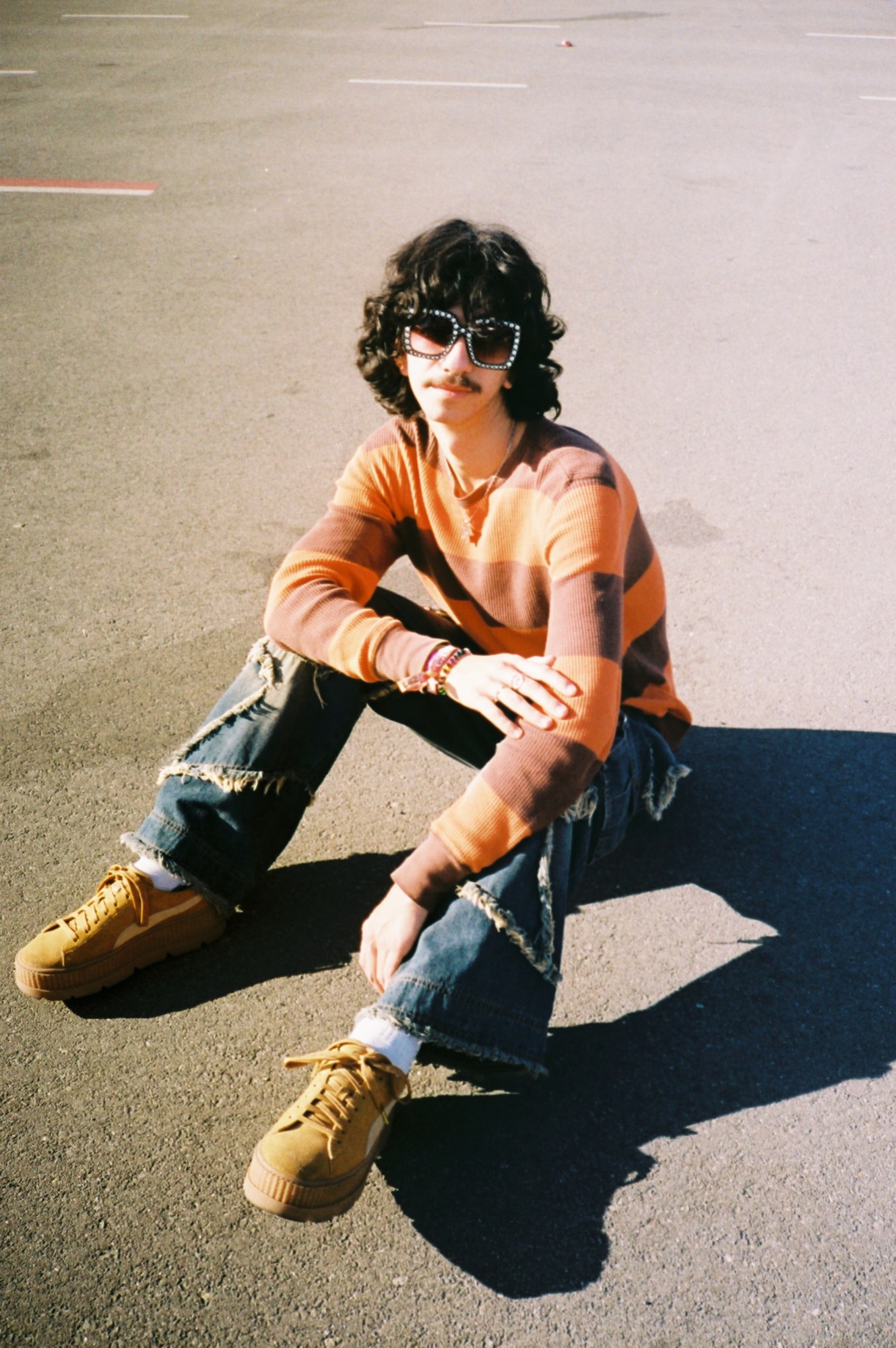 ben g wearing black rhinestone glasses and a striped sweater sitting in a parking lot