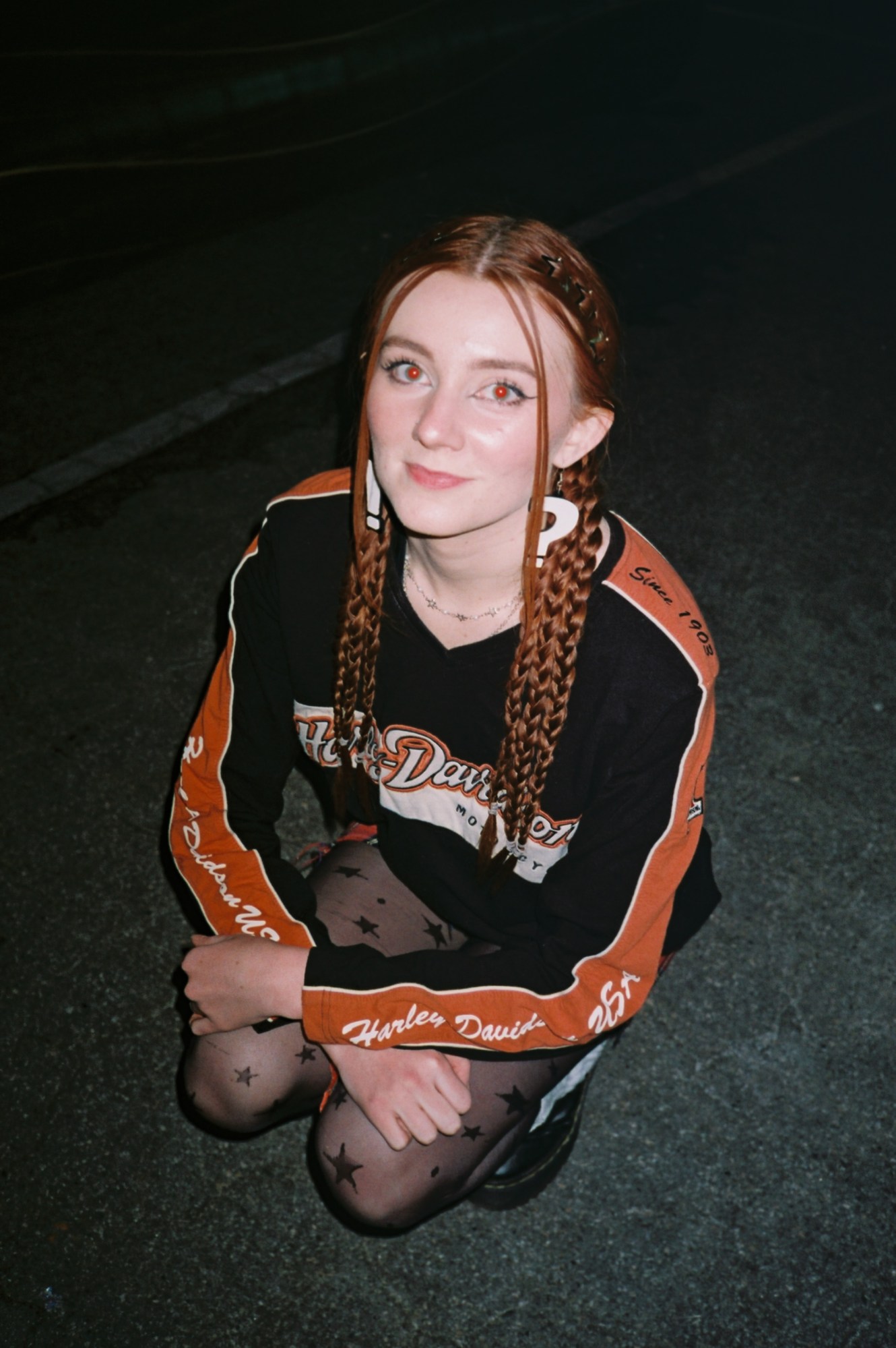 a girl sitting on the ground in star tights and a halrley davidson top at a music festival