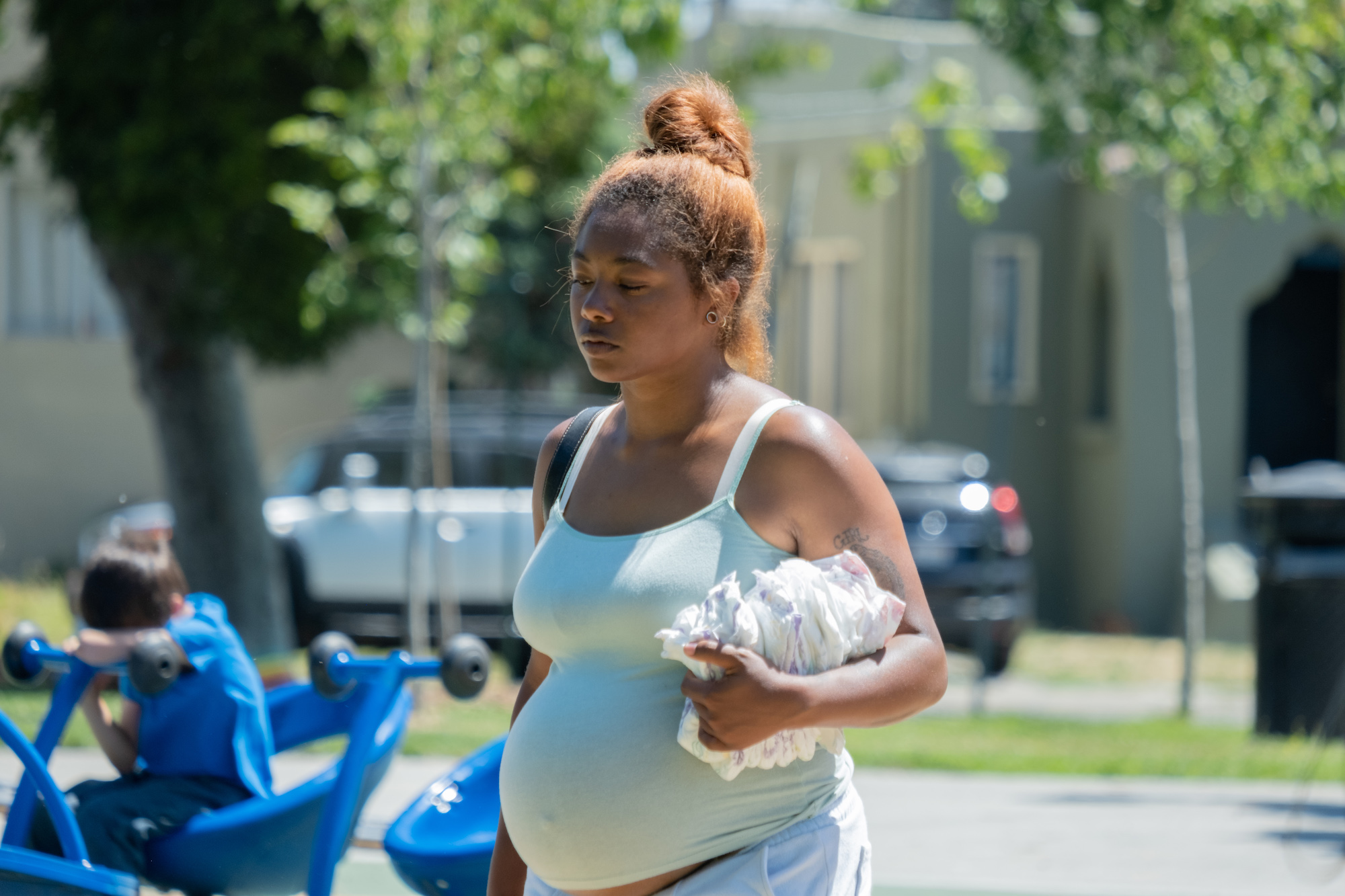 a pregnant young woman in a baby blue tank top carries a stack of diapers