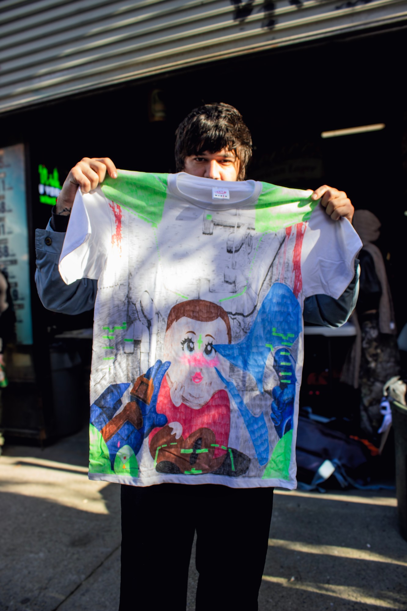 ryan holding up a colorful handrawn tshirt outside of a market in brooklyn