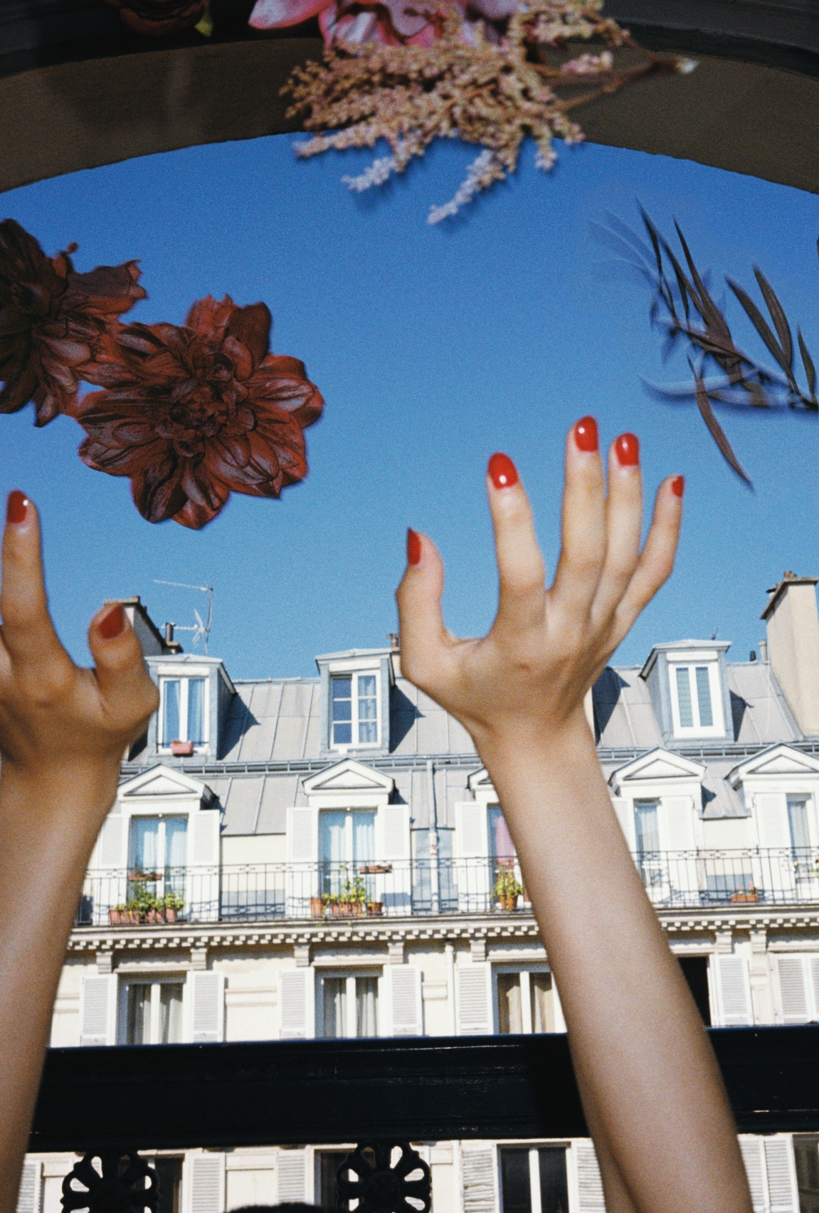 two hands with red nails reach towards a blue sky with apartments in the distance