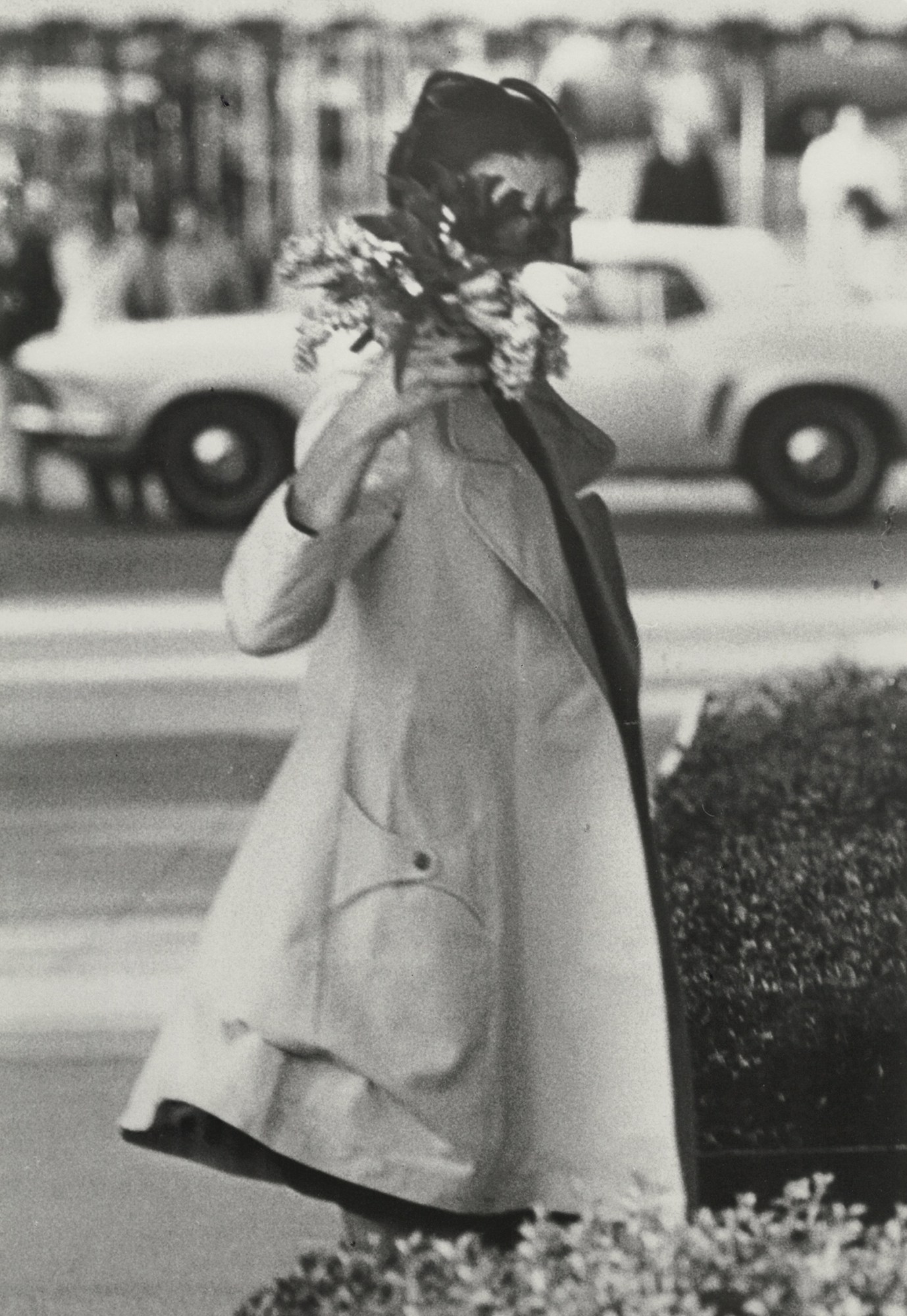 Jackie Onassis wearing a trench coat holding a bunch of flowers in front of her face