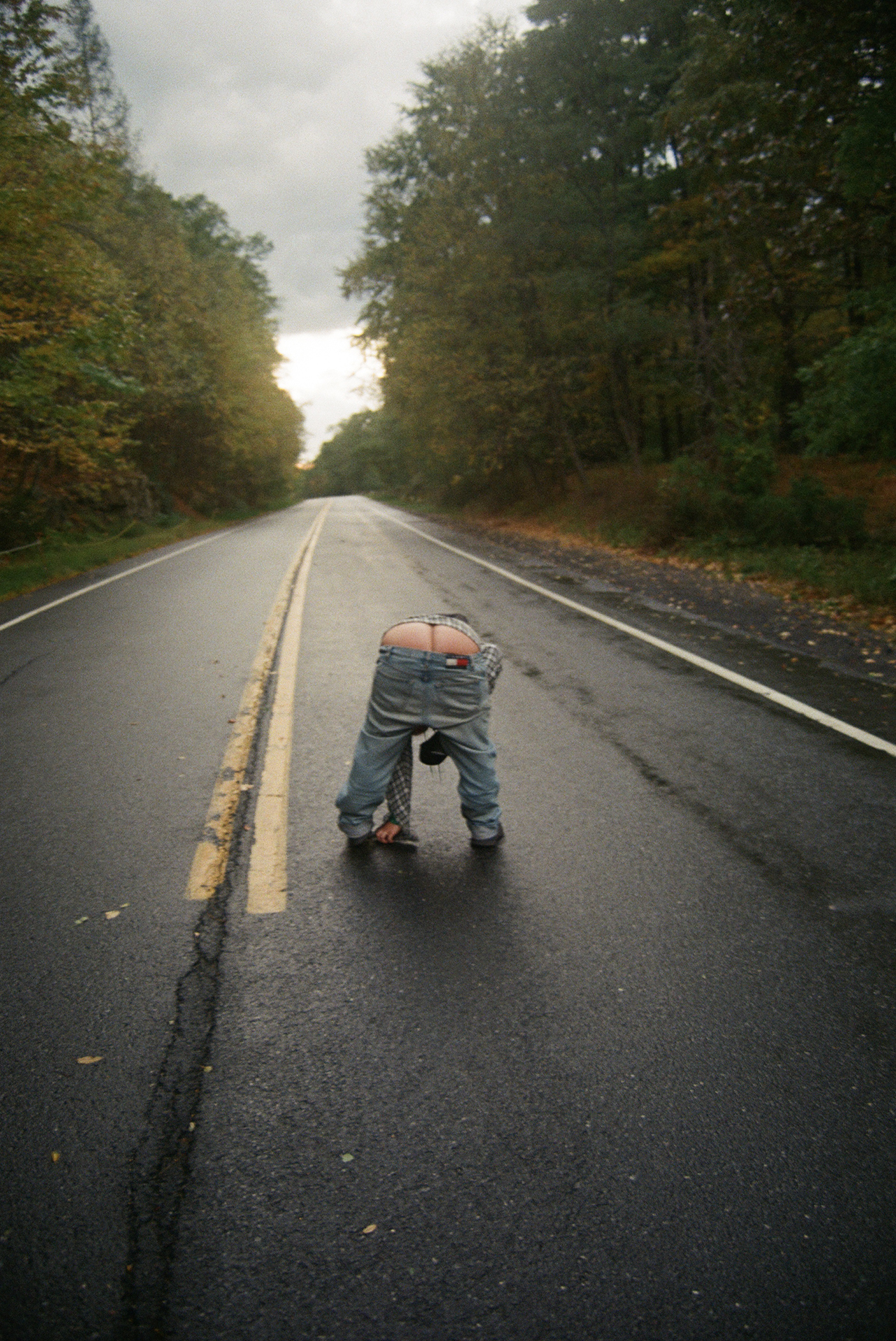 on a clear road at dawn, someone wearing blue denim pulls their jeans and trousers down and moons the camera