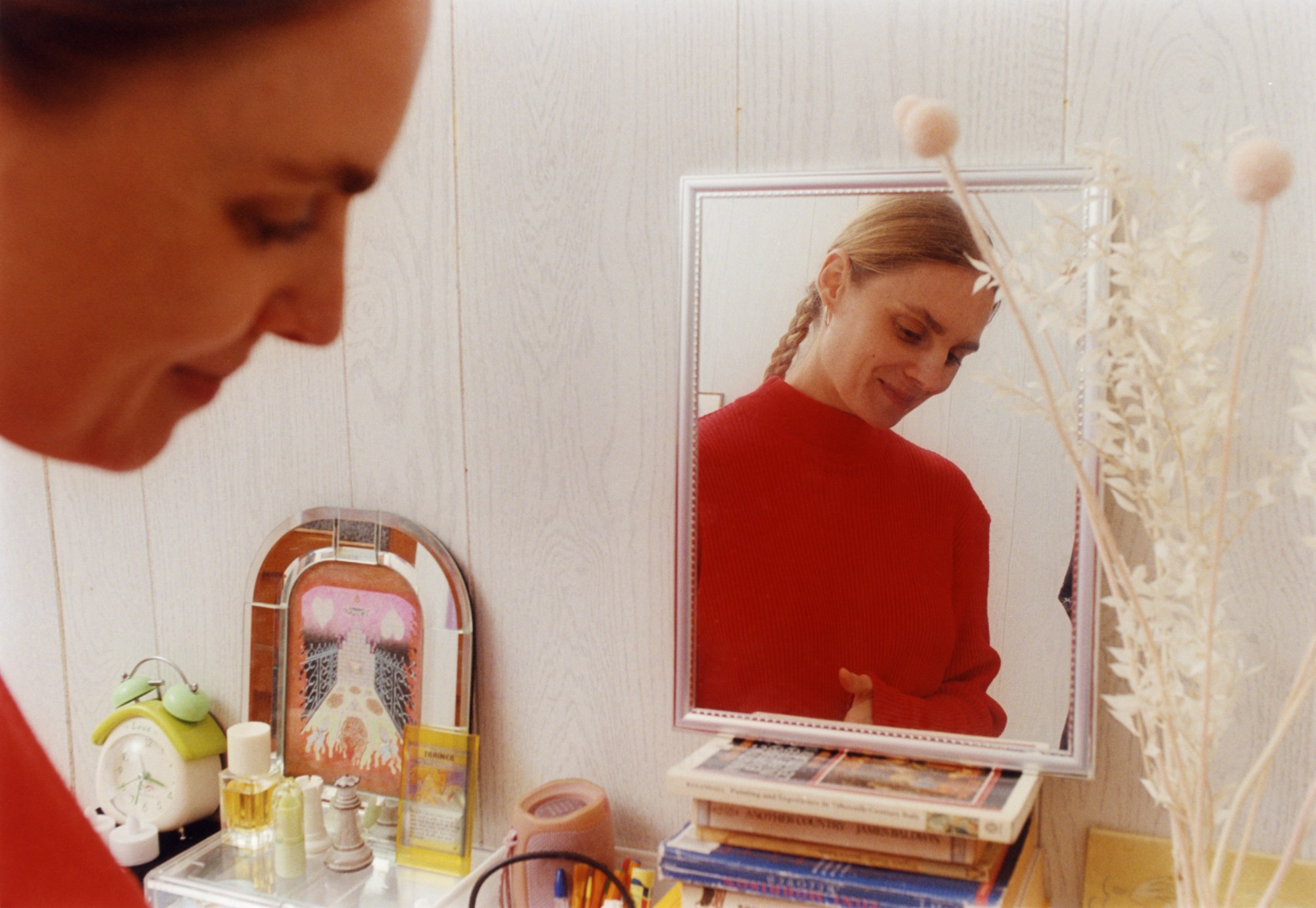 gitte maria moller in the foreground and reflected in a mirror on her dressing table; her perfume and a framed artwork sits nearby