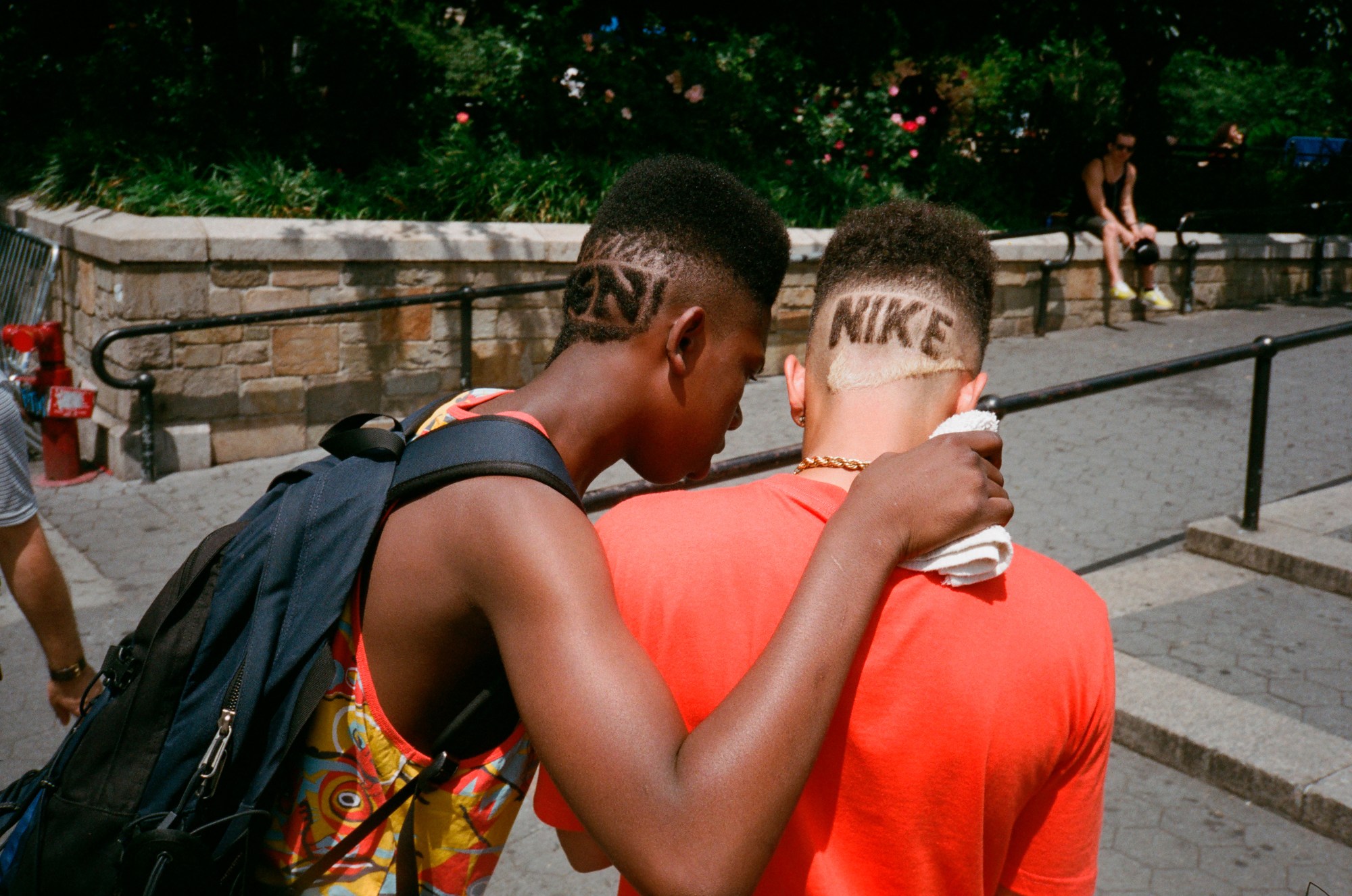 two teenage boys photographed from behind with nike logos and words shaved into the back of their heads. one looks over the other's shoulder at a phone.