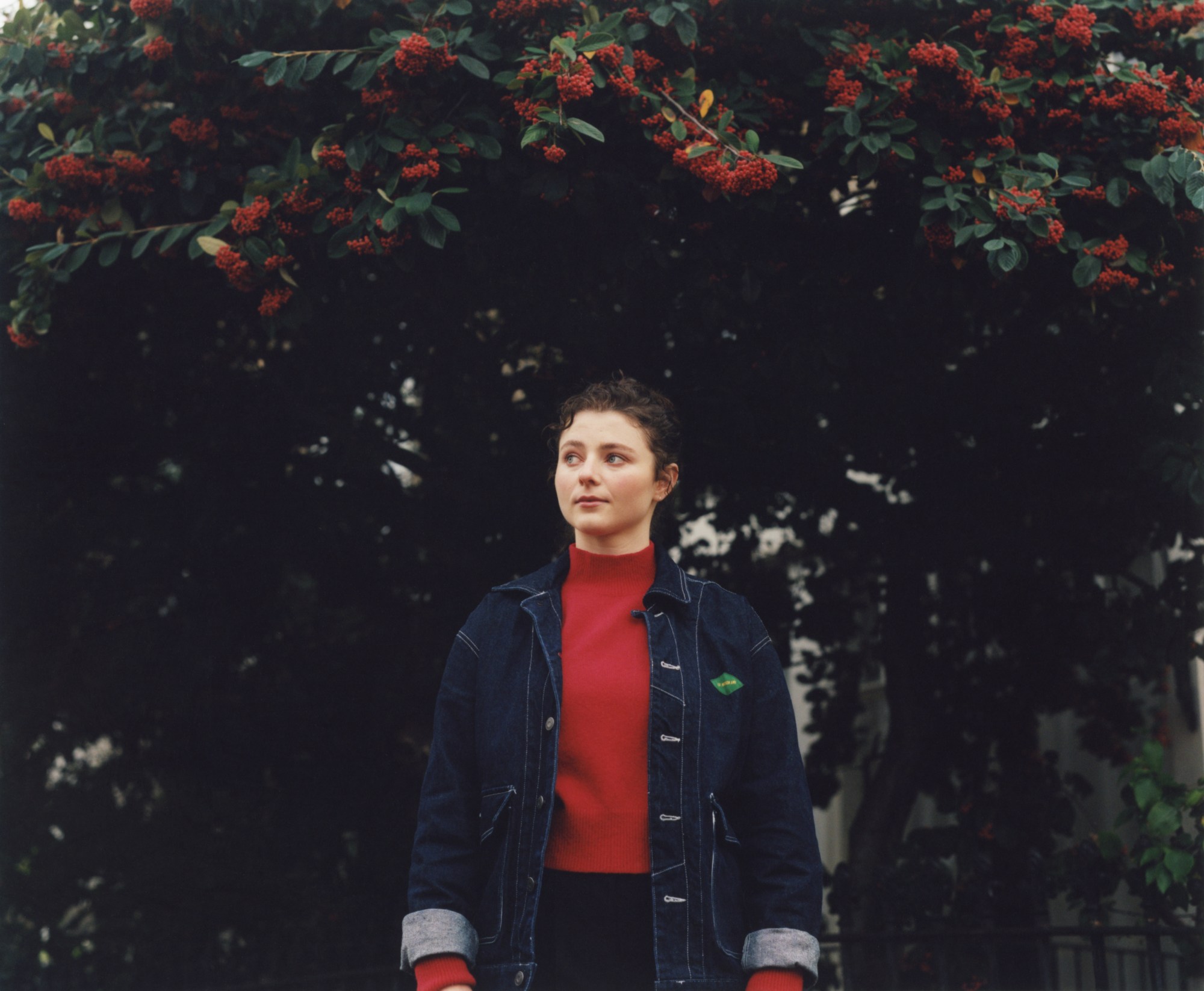 actor thomasin mckenzie in a red sweater under trees