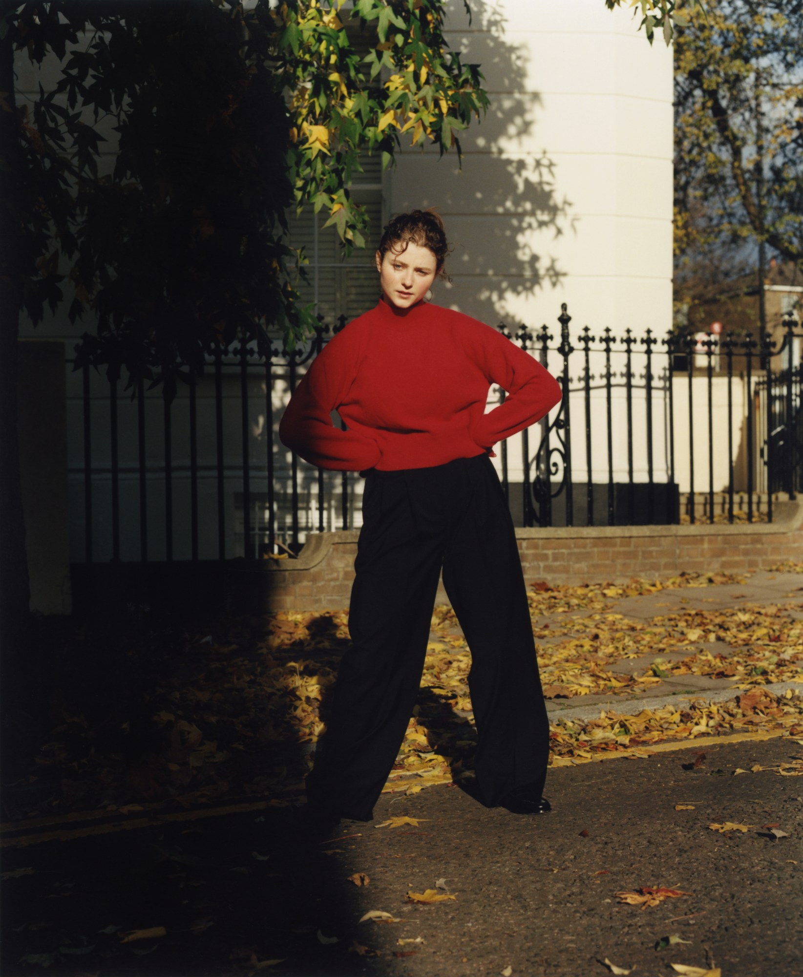 thomasin mckenzie standing on a leaf covered street in london posing with her hands on her hips