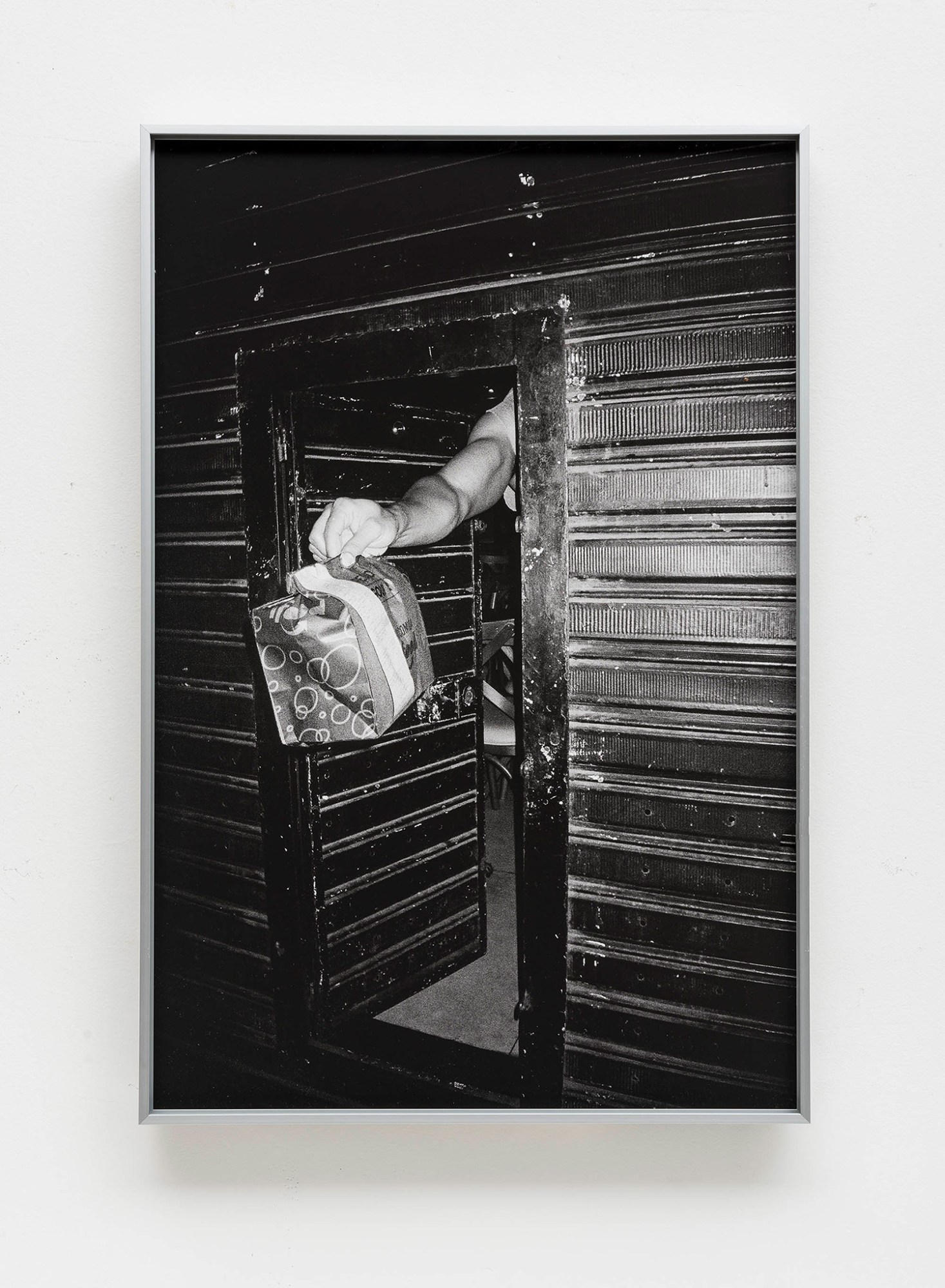 a b&w photograph of an arm sticking out of a door holding a paper food delivery bag