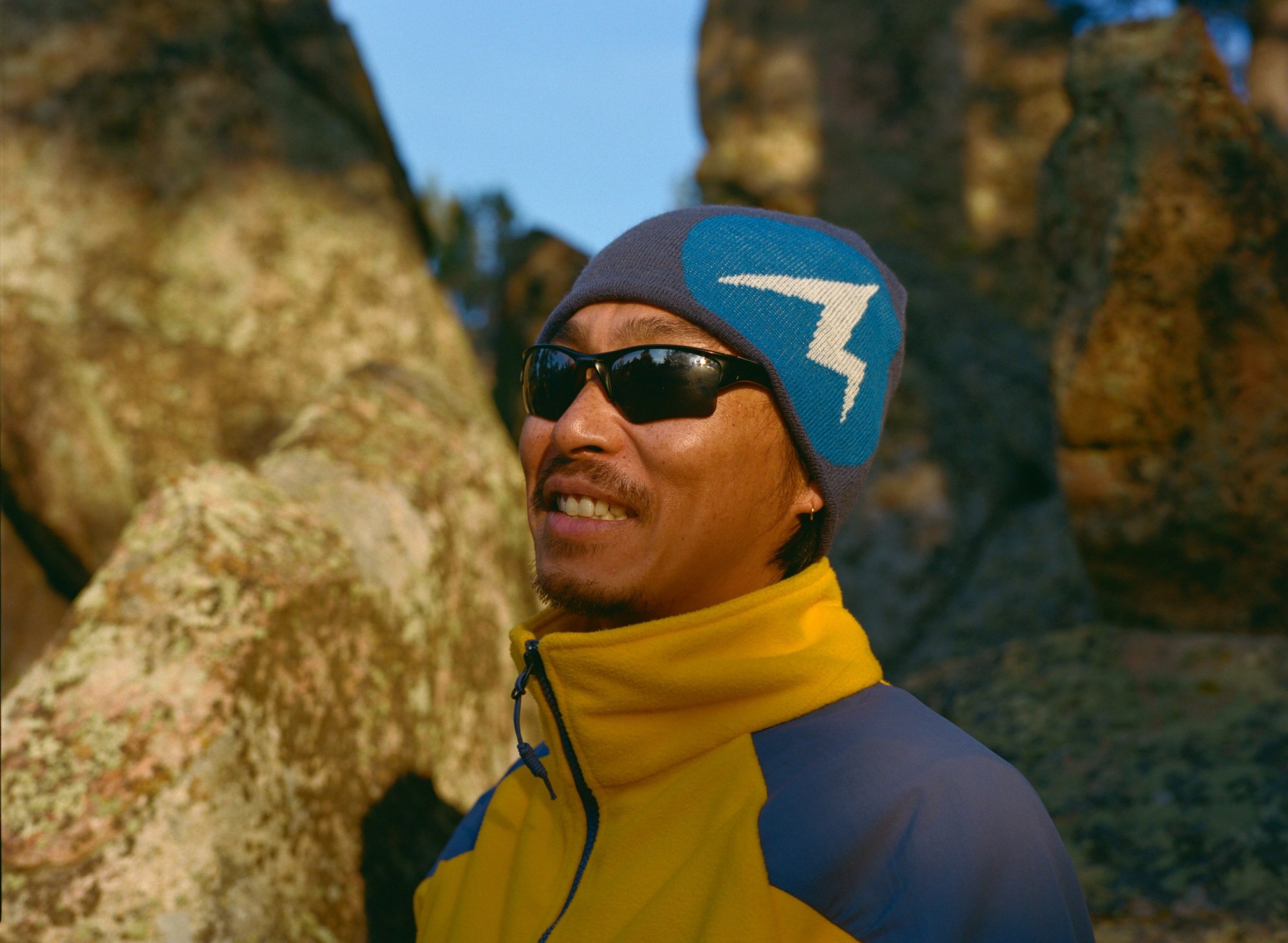 a man wearing a marmot beanie and yellow zip up and glasses outdoors