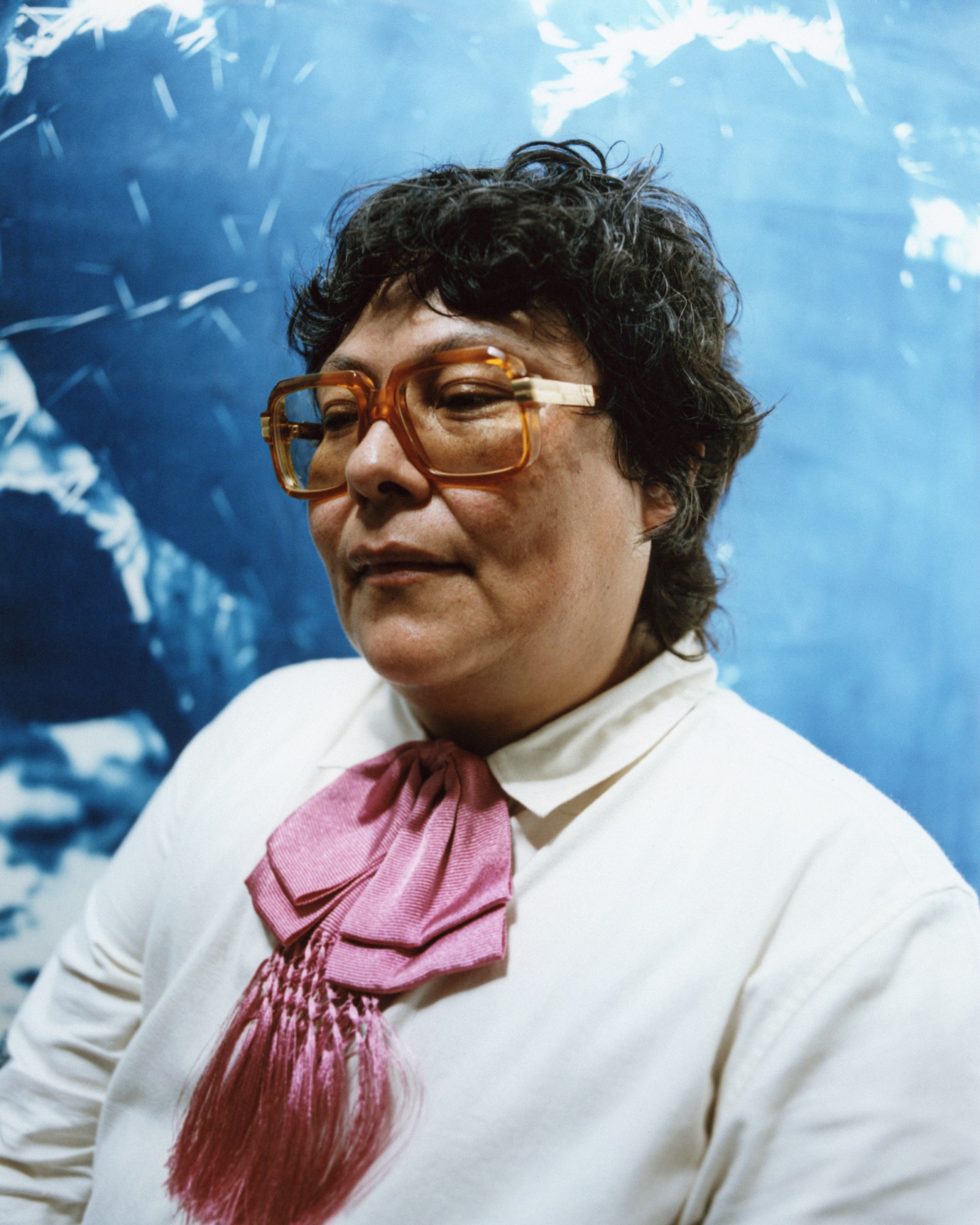 amina cruz in glasses and a pink bow tie in front of a blue painting