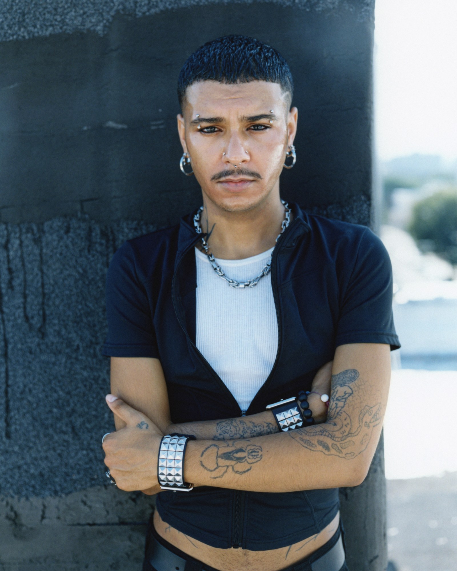 juan lopez on a rooftop in a black zip up and studded jewelry