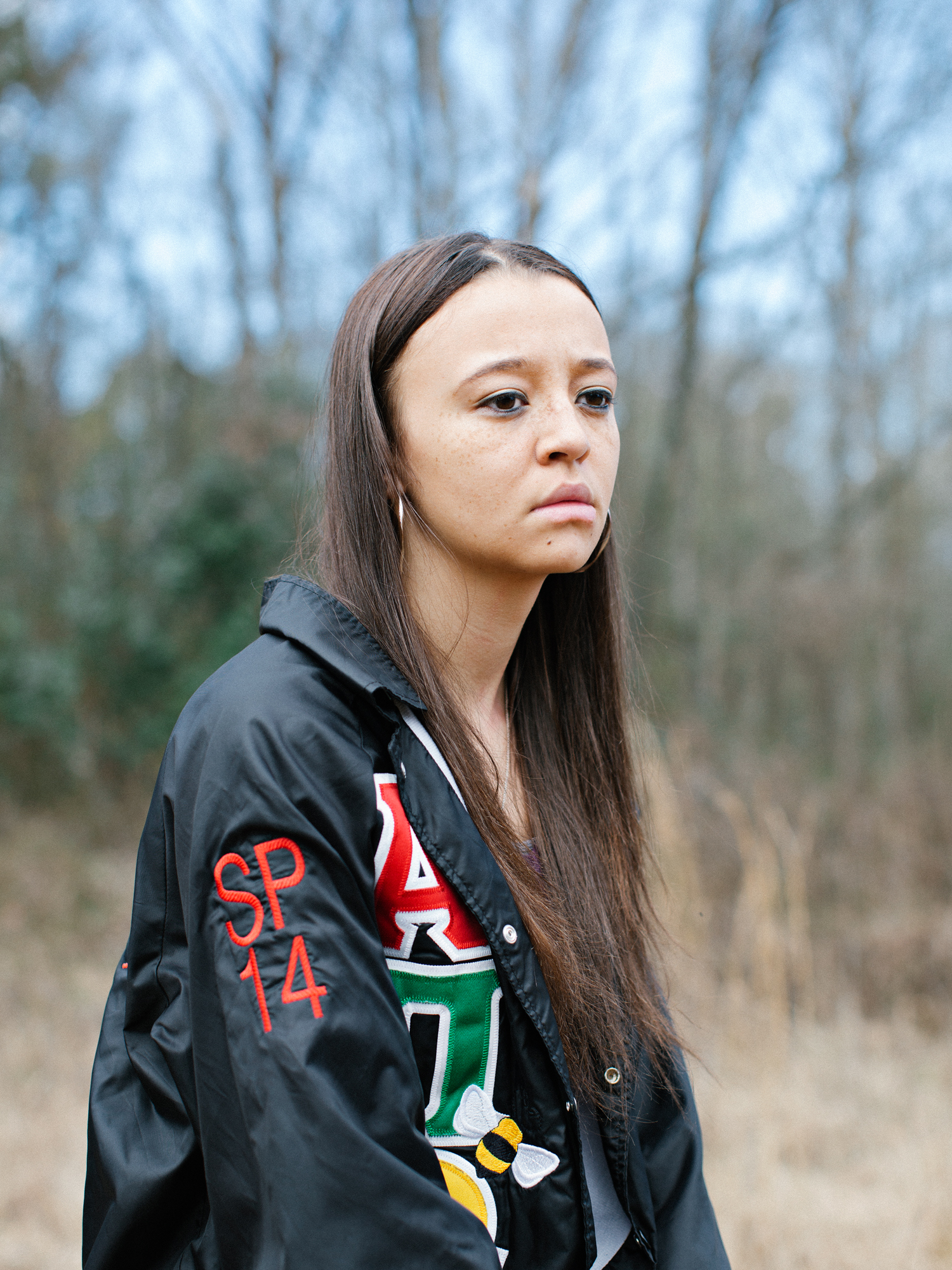 Jasmine wearing a black embroidered sorority jacket in a field outside