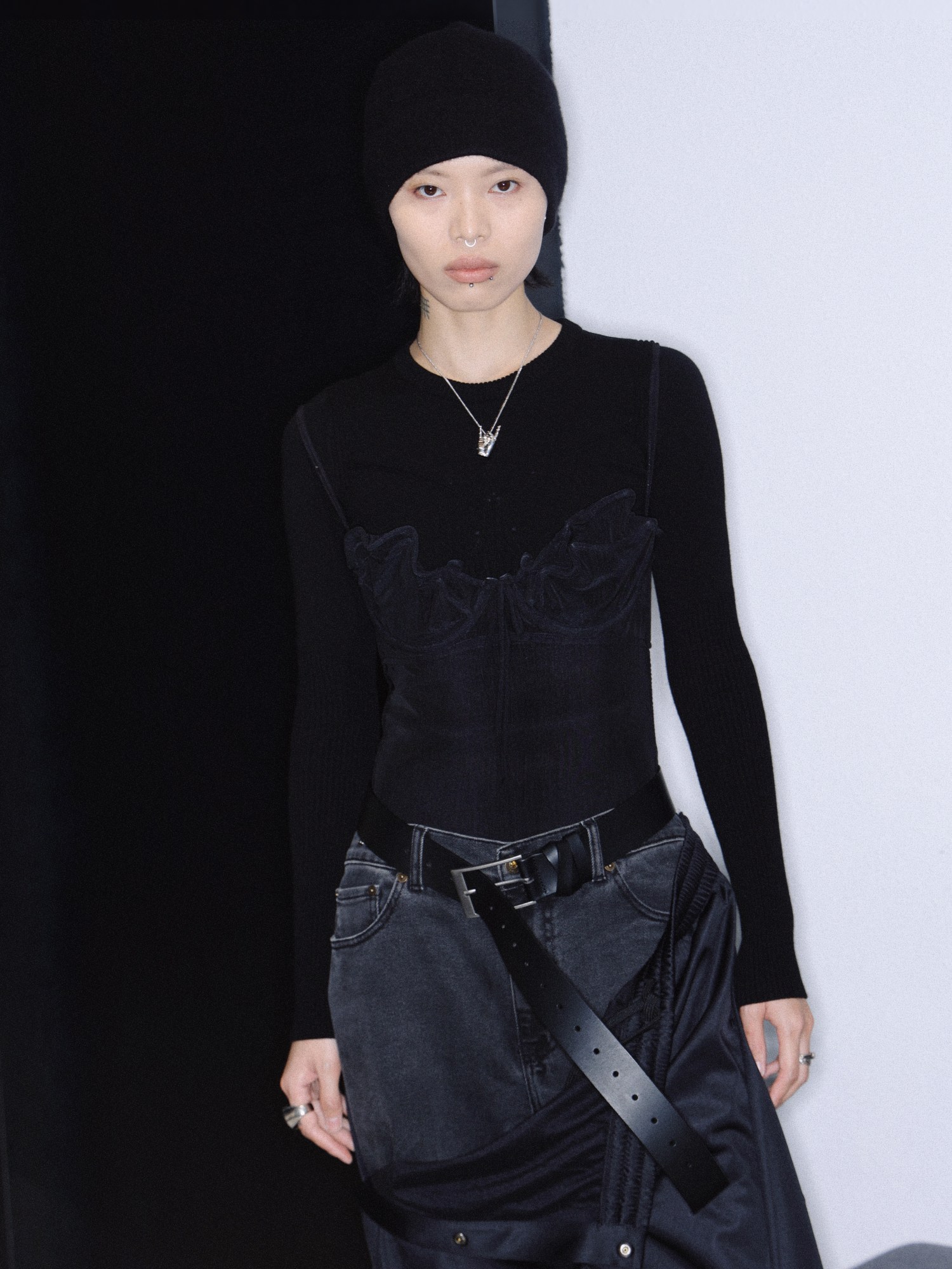 a woman wears baggy black jeans, a bustier over a long thermal top and a beanie over her short hair