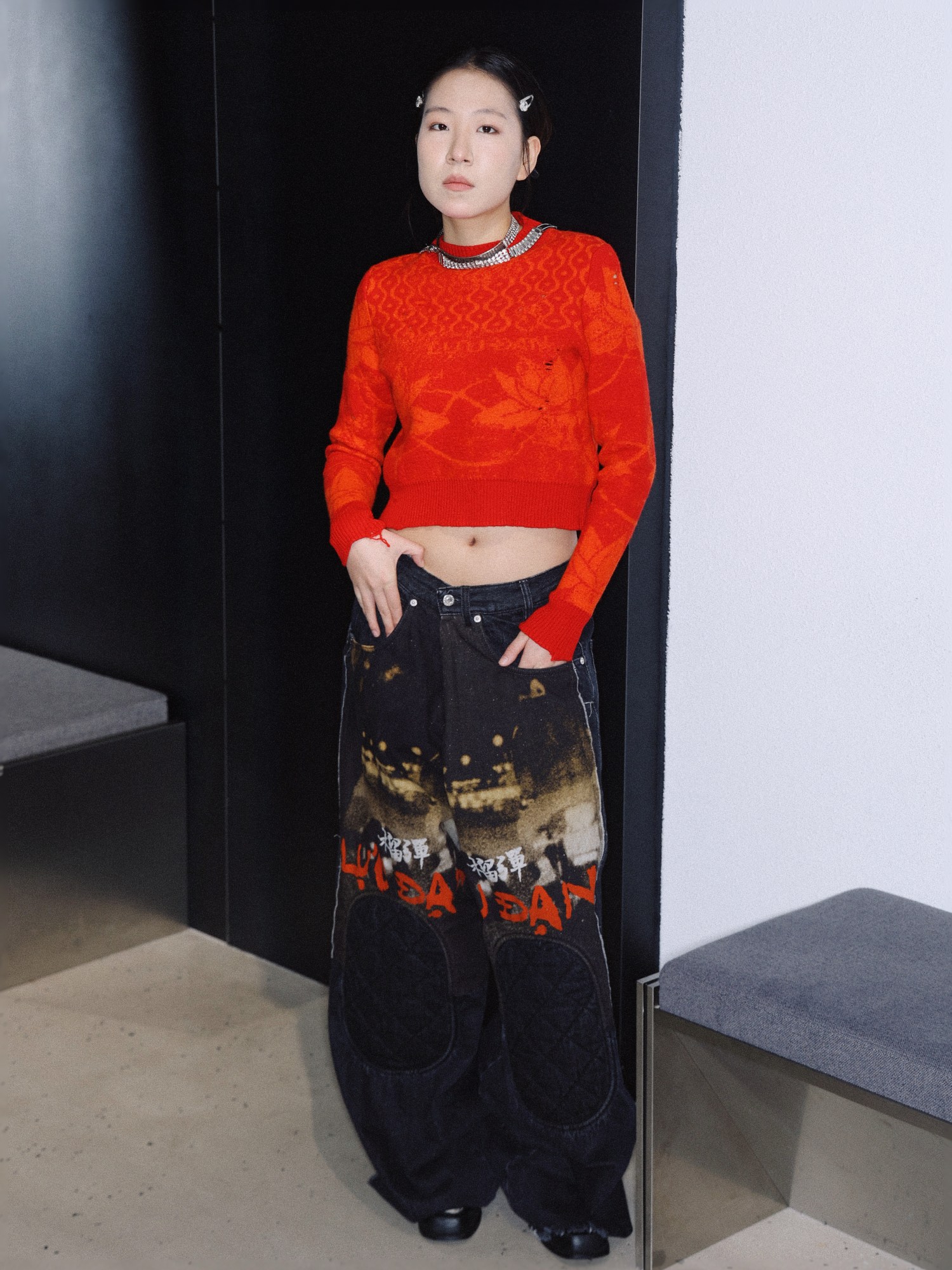 a woman in patterned jeans and a cropped red sweater wears a silver chain and hairclips