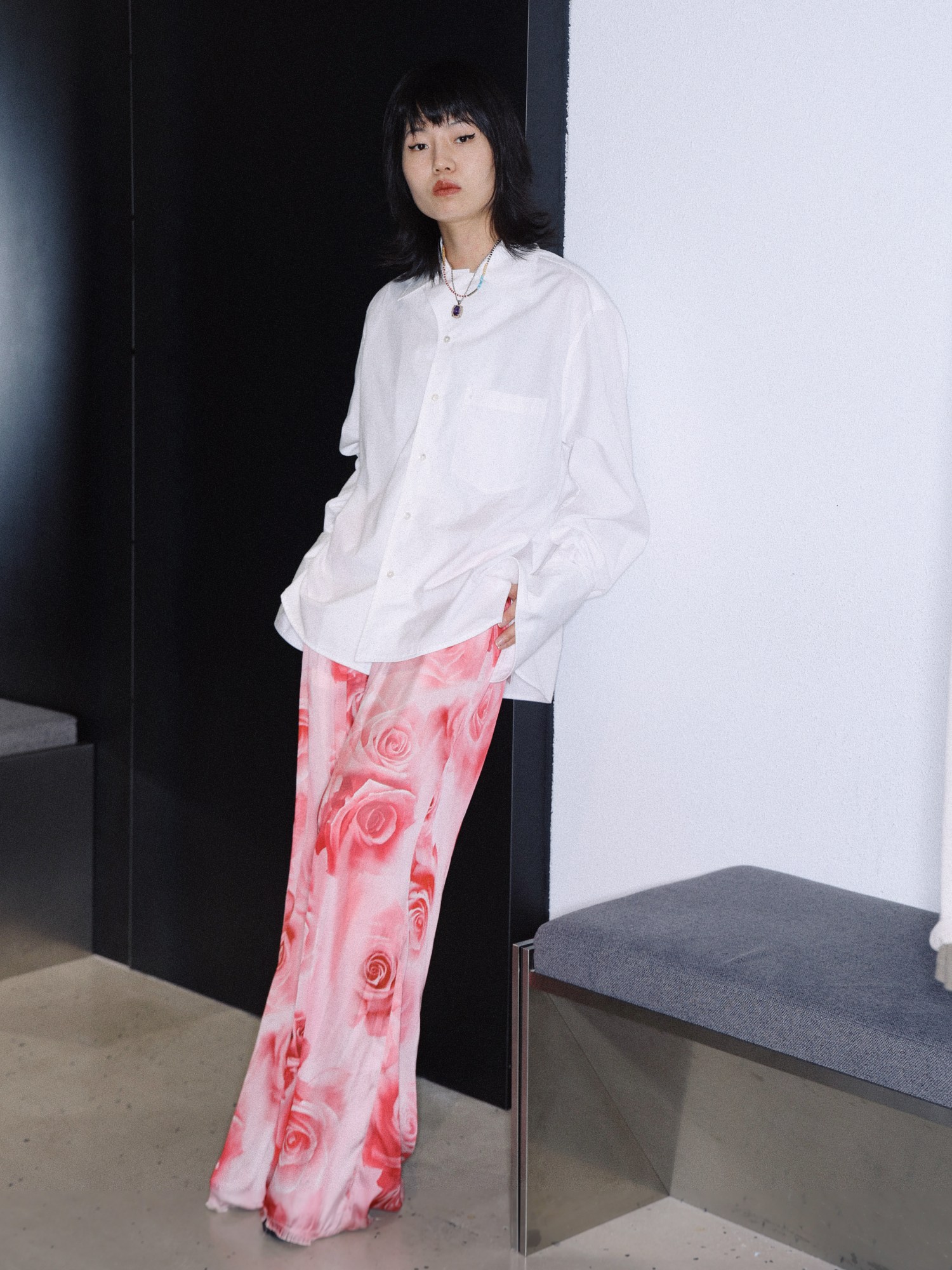 a woman in a long rose print skirt and white shirt leans against a wall in a shop