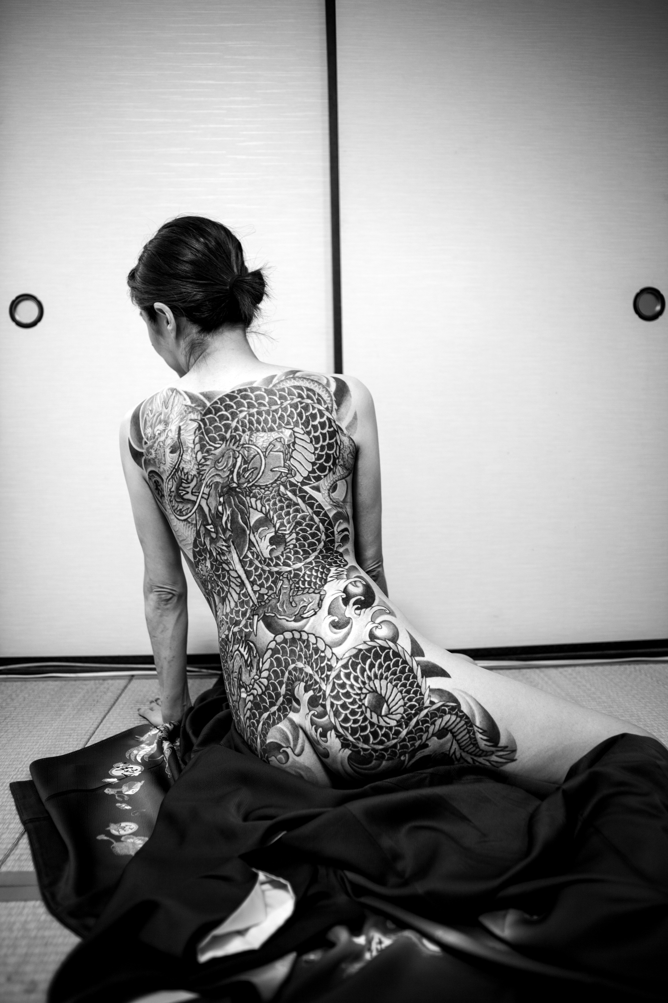 black-and-white image of a naked woman facing away from the camera, her back covered with traditional japanese tattoos