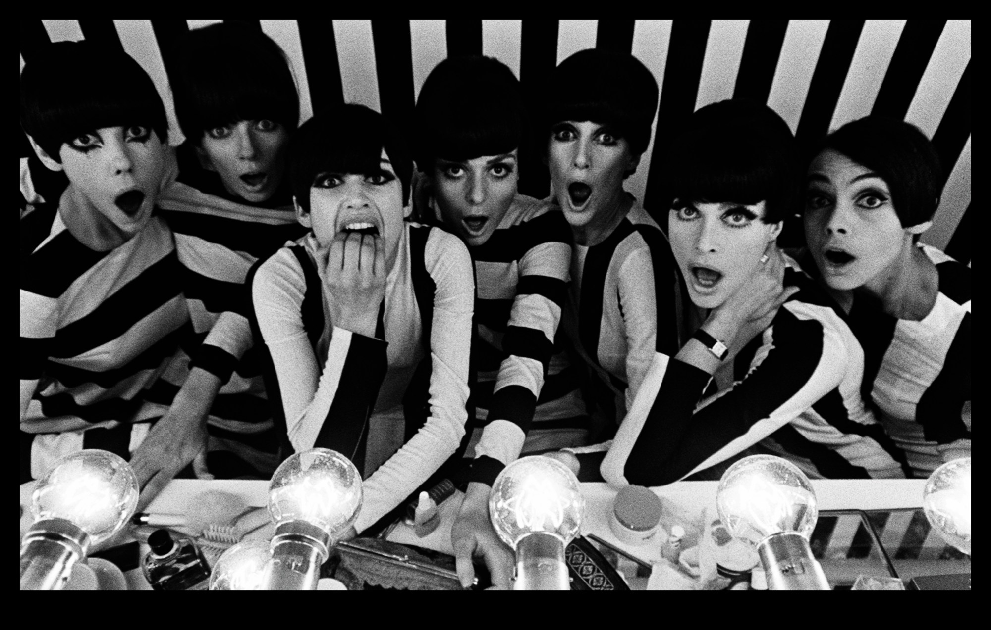 black-and-white photo of seven showgirls in monochrome vertical stripes circa 1960s