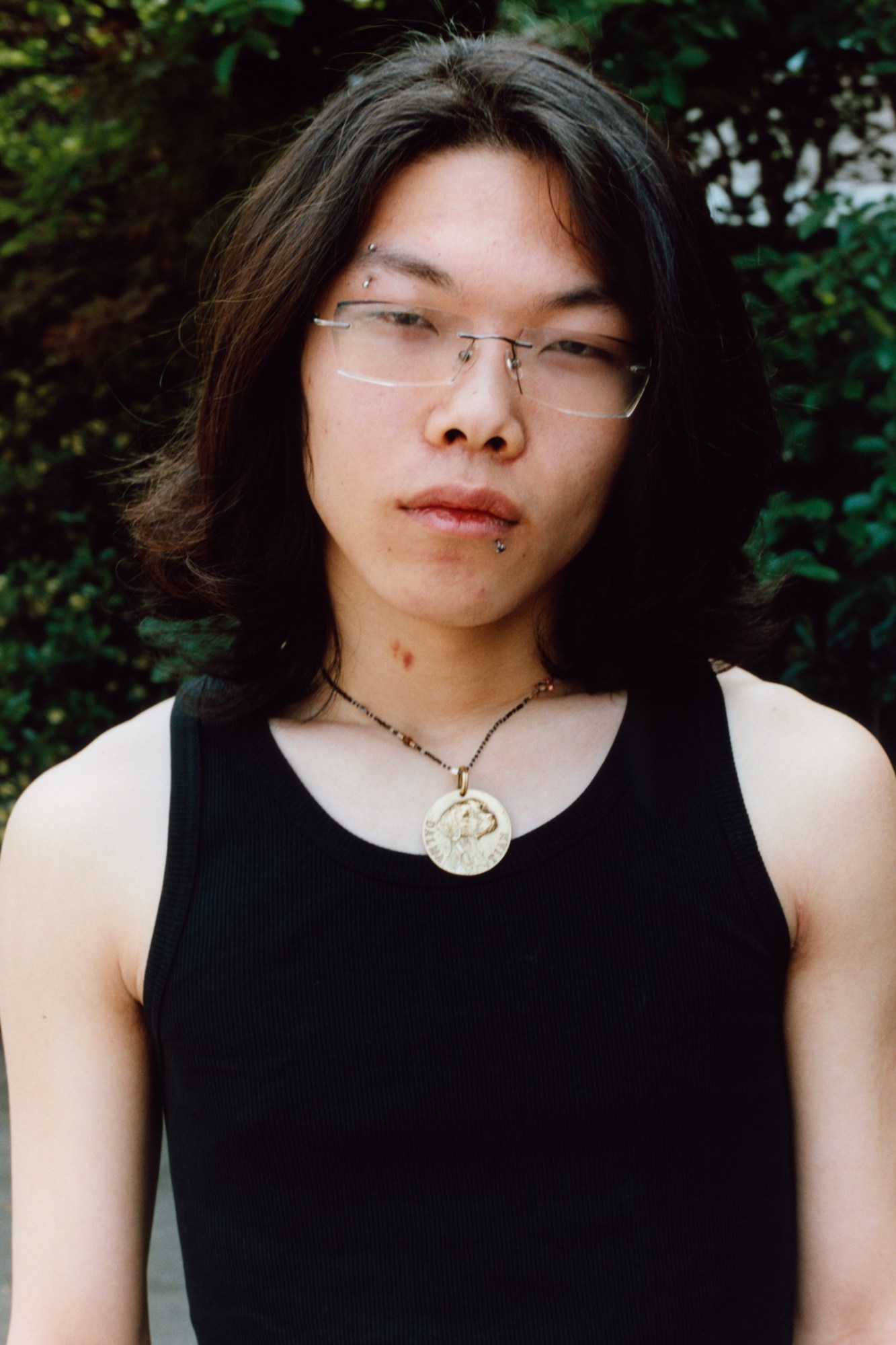 a young man in a black tank top wearing rectangular glasses