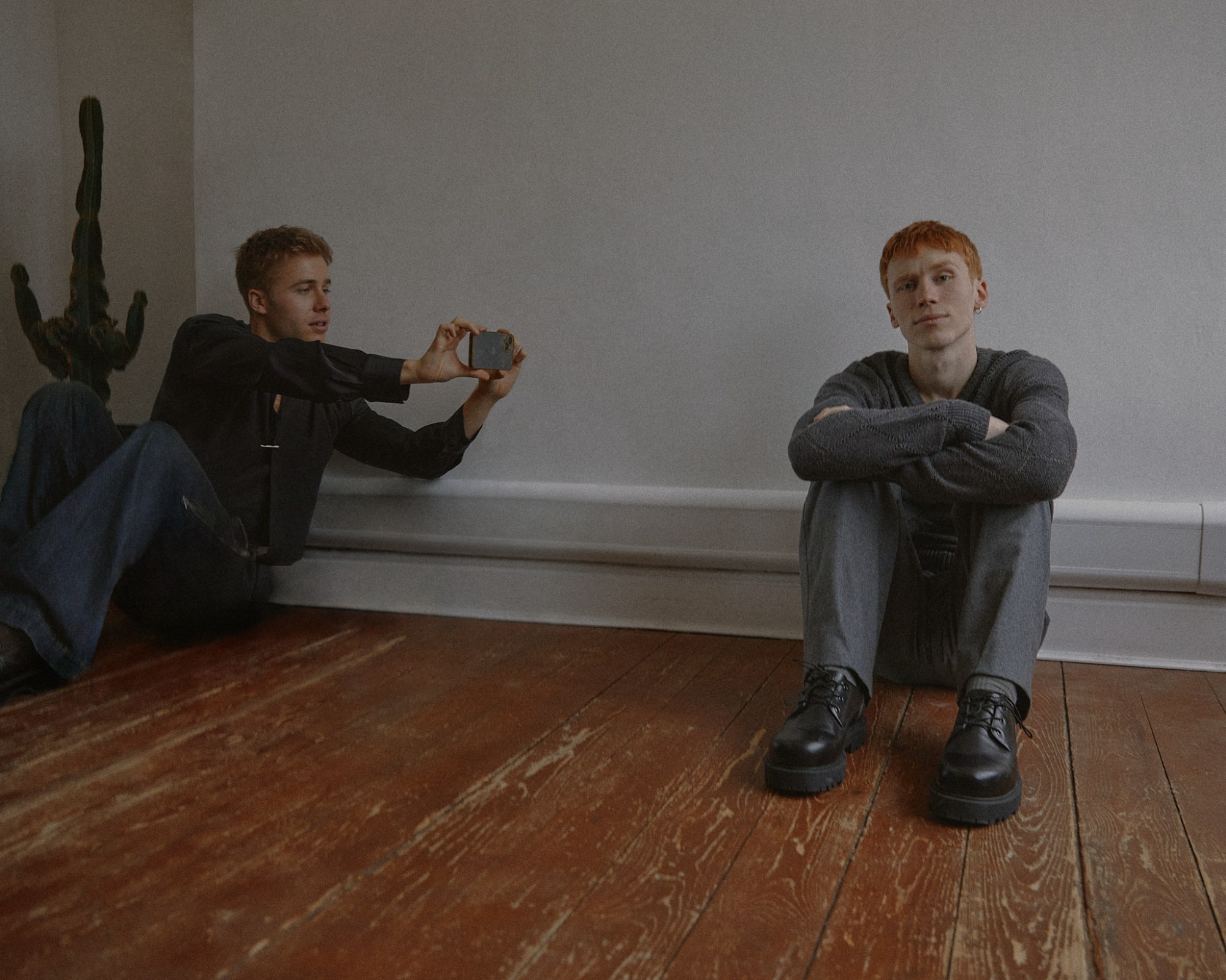 luther ford and ed mcvey actors sitting on the floor against a white wall. ed takes a photo of luther posing.