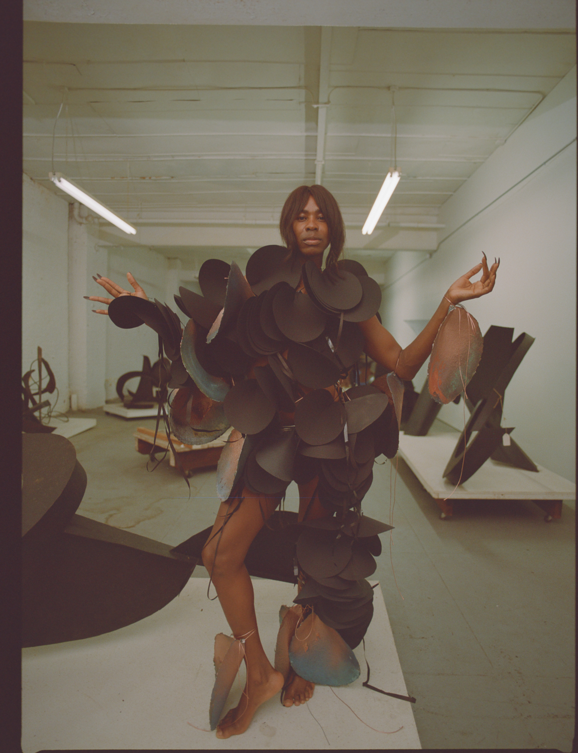 emani standing among black sculptures in a paper gown by karina sharif