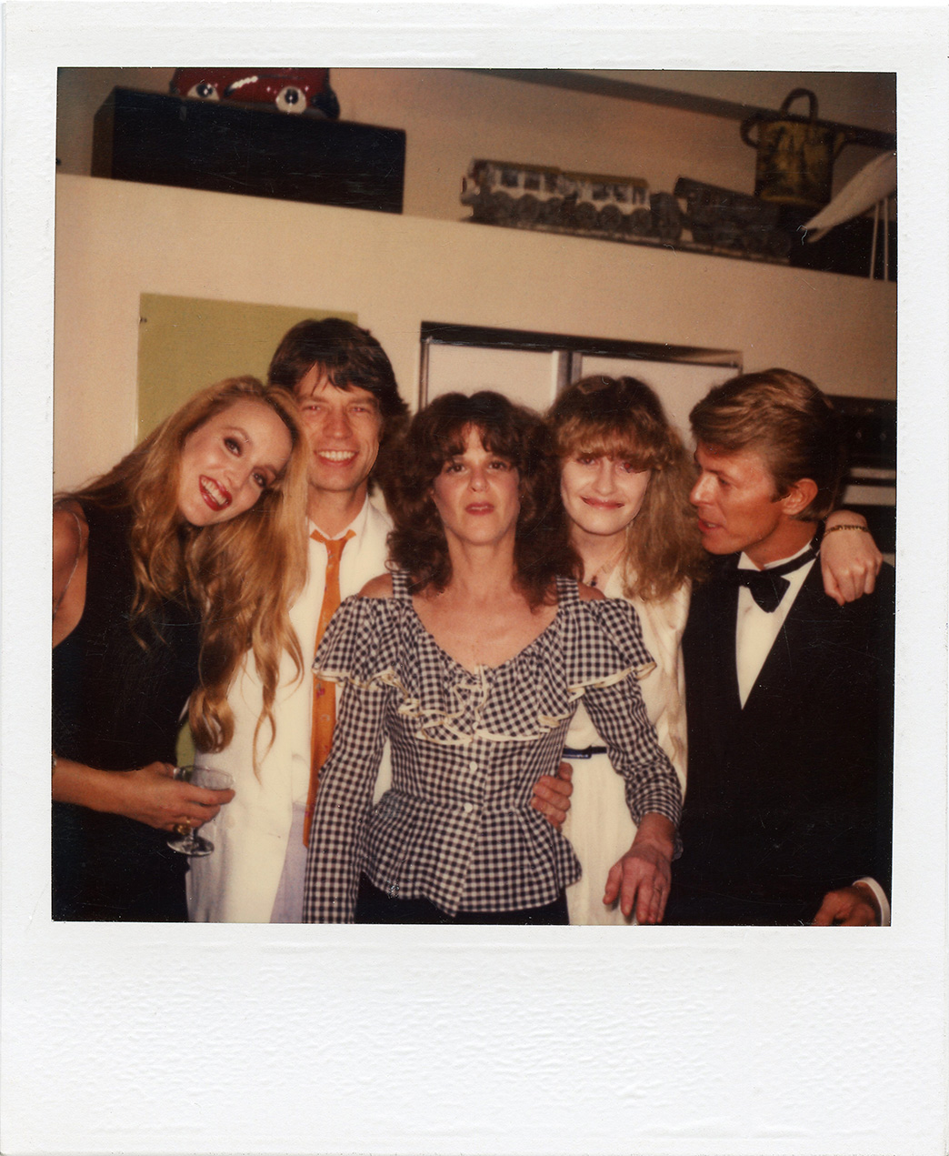 jerry hall, mick jagger, david bowie and friends gather round for a polaroid at a house party in the 70s