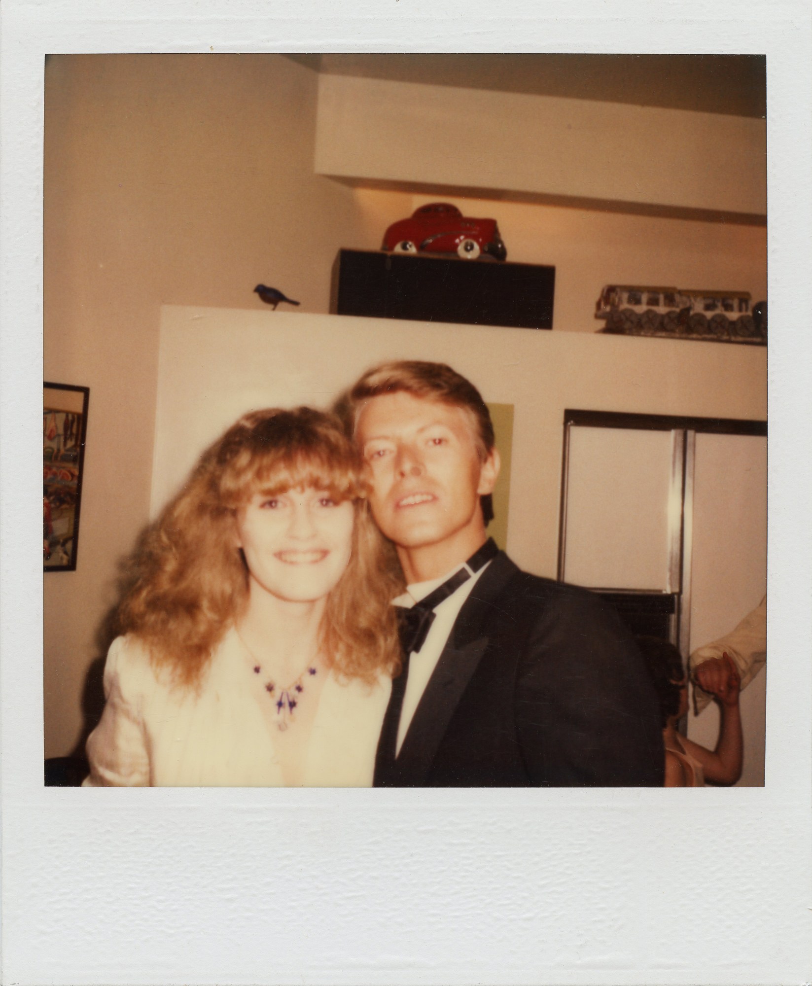 david bowie and a friend smile for a photograph at a party; they're dressed formally and the image is sepia-toned