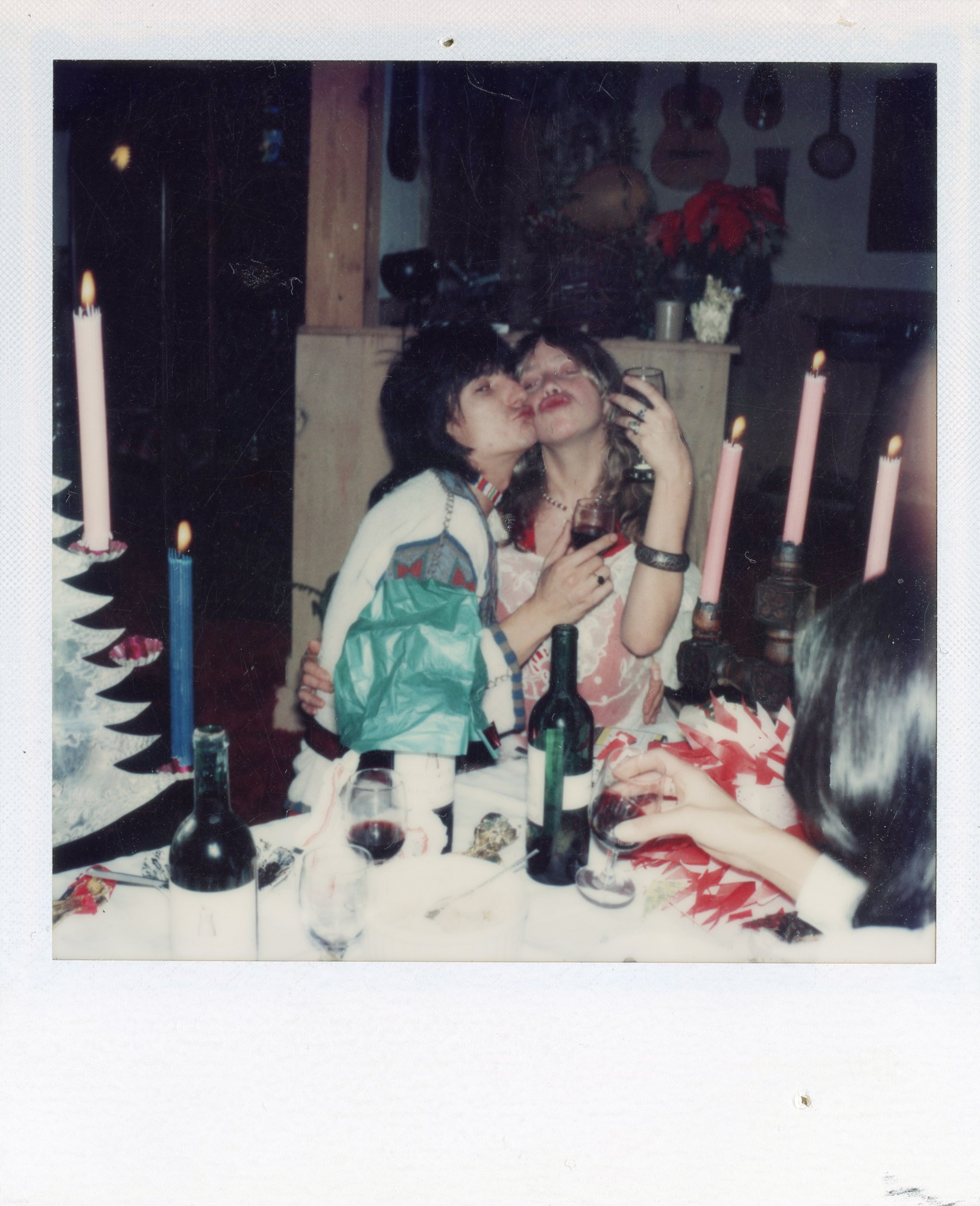 ronnie wood and a friend raise their glasses while pouting for the camera behind a table covered in christmas decorations and lit candles