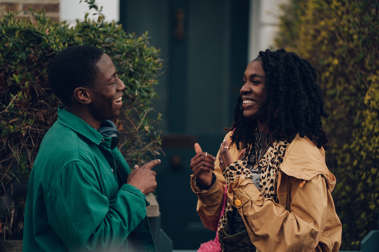 a still of the lead characters in 'rye lane' standing outside a house smiling at each other