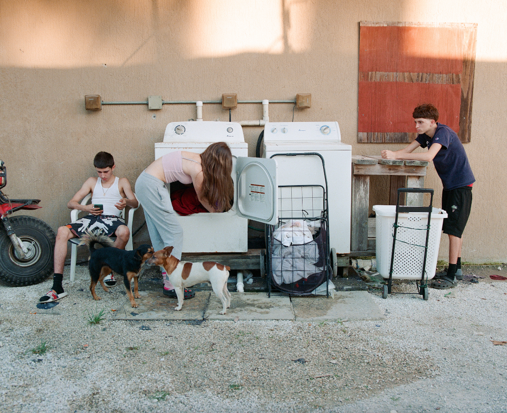 Photograph by Giovanni Mourin of three people and two dogs by washing machines in South Beach Miami from Homestead