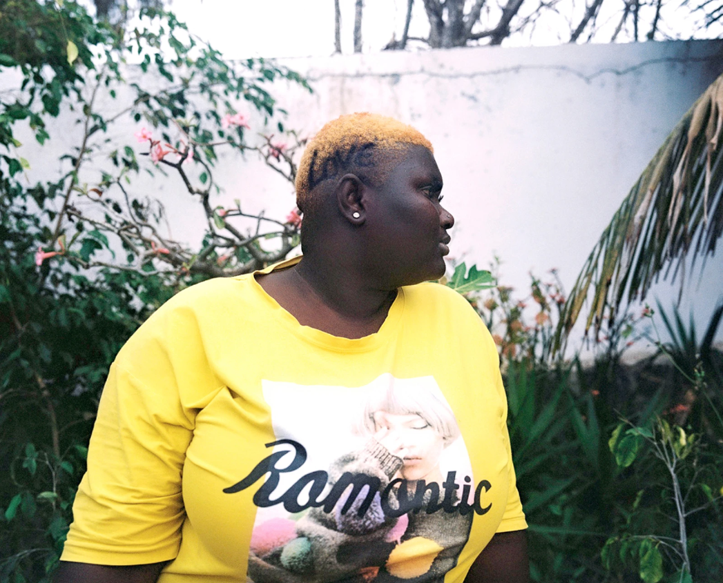 Photograph by Charlotte Yonga of a woman in senegal in a yellow top in a garden