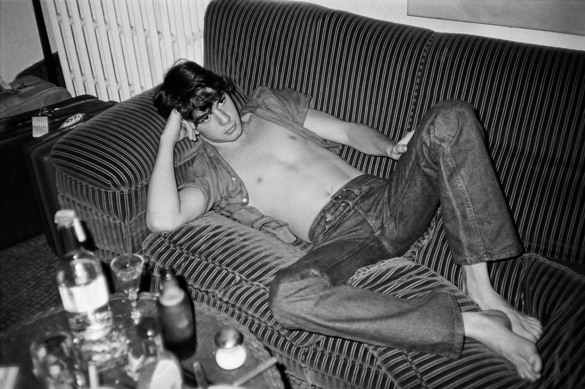 Photograph by Patrick McMullan of a boy in jeans and a shirt on a sofa with alcohol on a table next to him