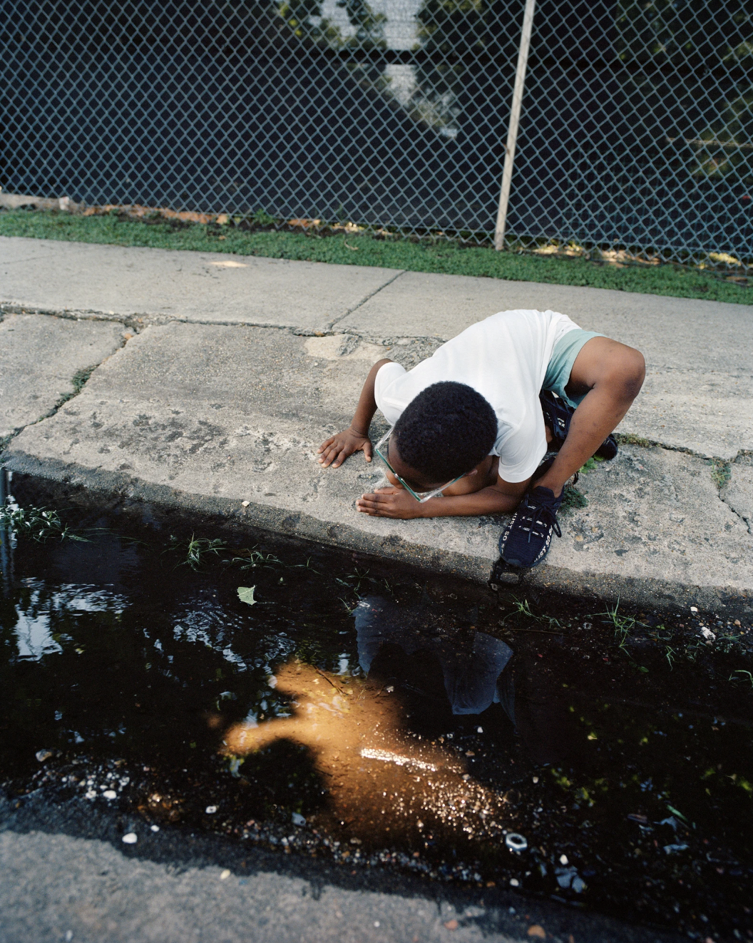 Photograph by Vasantha Yogananthan of a boy on the side of a street looking into a puddle from the series 'Mystery Street'