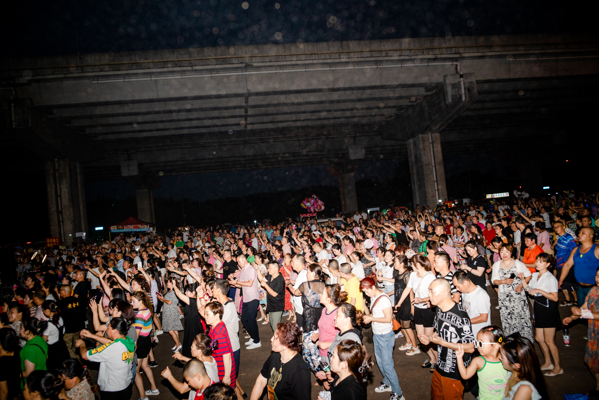 hundreds of chinese people dancing at a rave under a highway