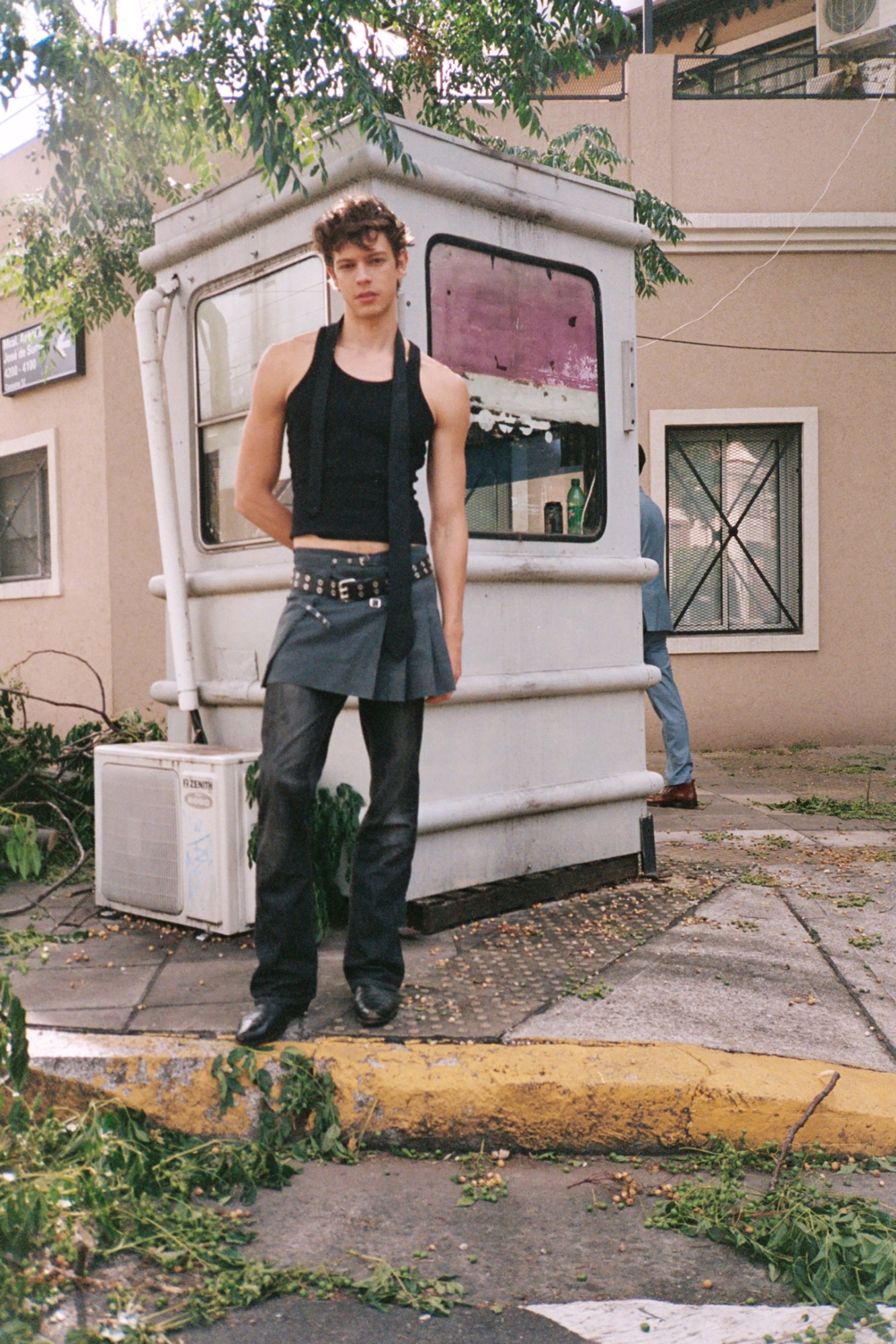 a model wearing a black tank top and a short kilt over jeans poses in a buenos aires street, in front of a cabin office