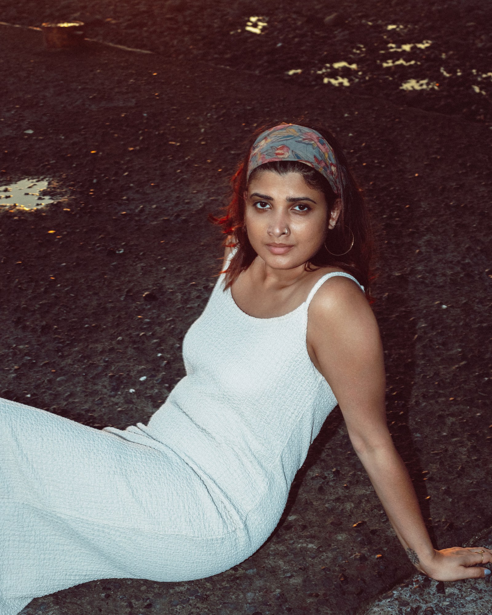 Indian All We Imagine as Light actor Divya Prabha, a brown Indian woman with shoulder length dark hair, wears a white slip dress and a paisley hair tie, sat on the ground.