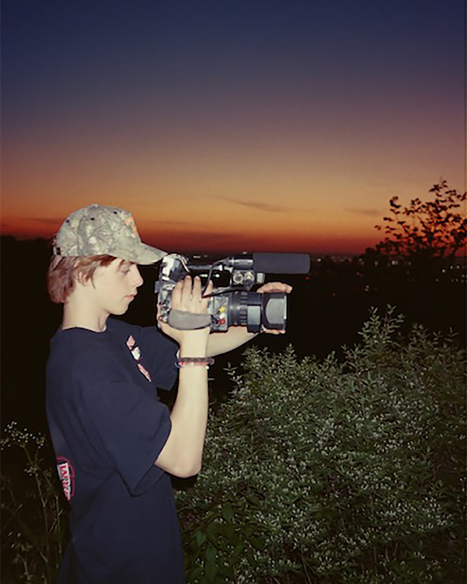 A young man holds a video camera at sunset