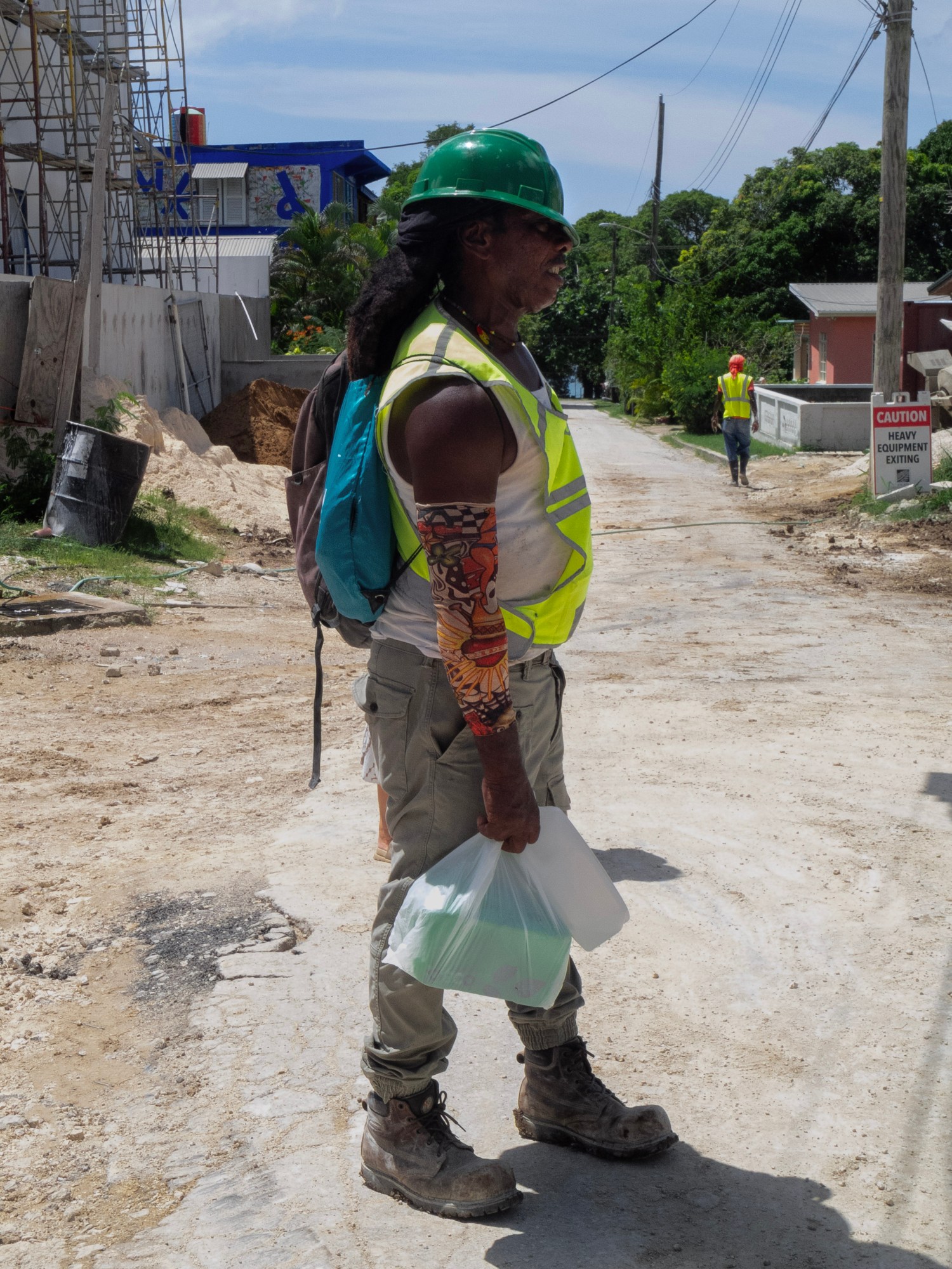 Man in hi-vis construction uniform, green helmet and arm sleeves stands side profile on a construction site.