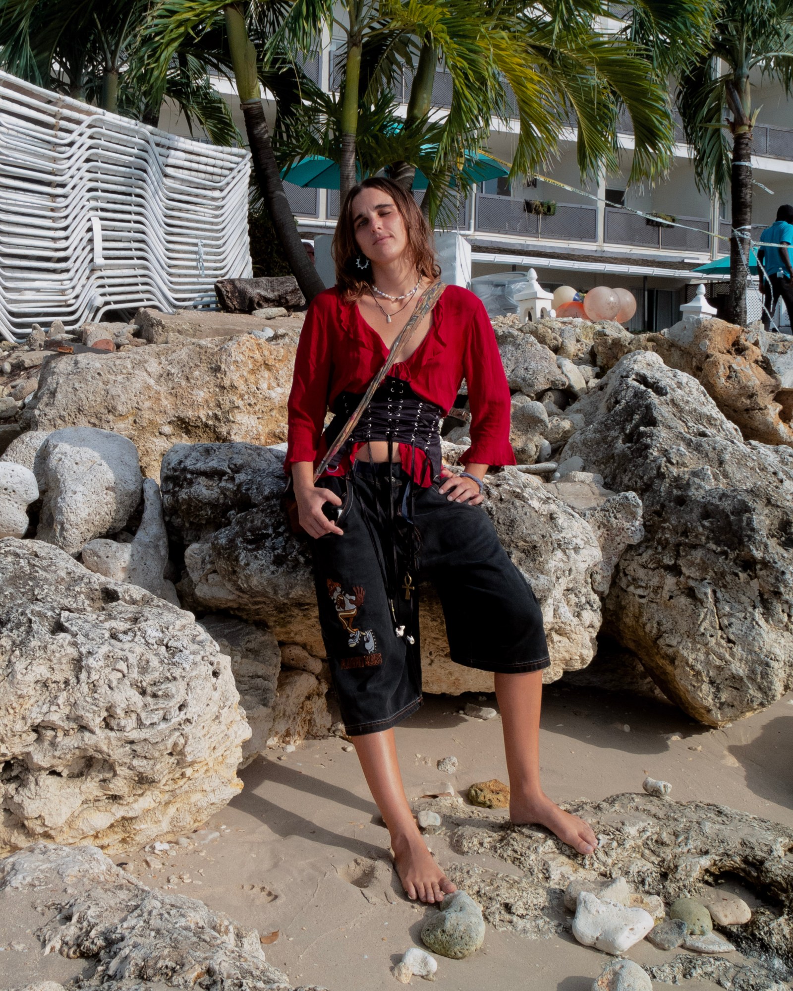 Woman in black bloomer pants and red top standing on the beach.